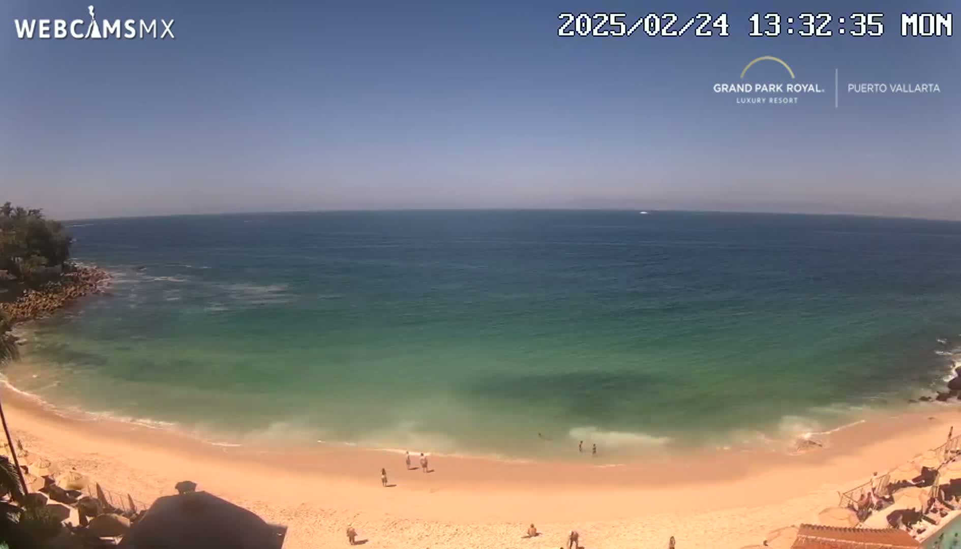 A sandy beach curves into a calm, teal ocean under a clear blue sky.