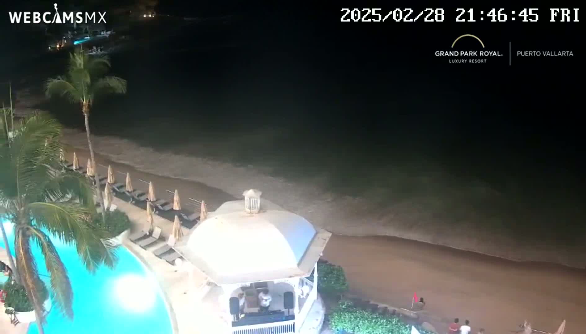 A nighttime view of a resort pool and beach with gentle waves lapping the shore.