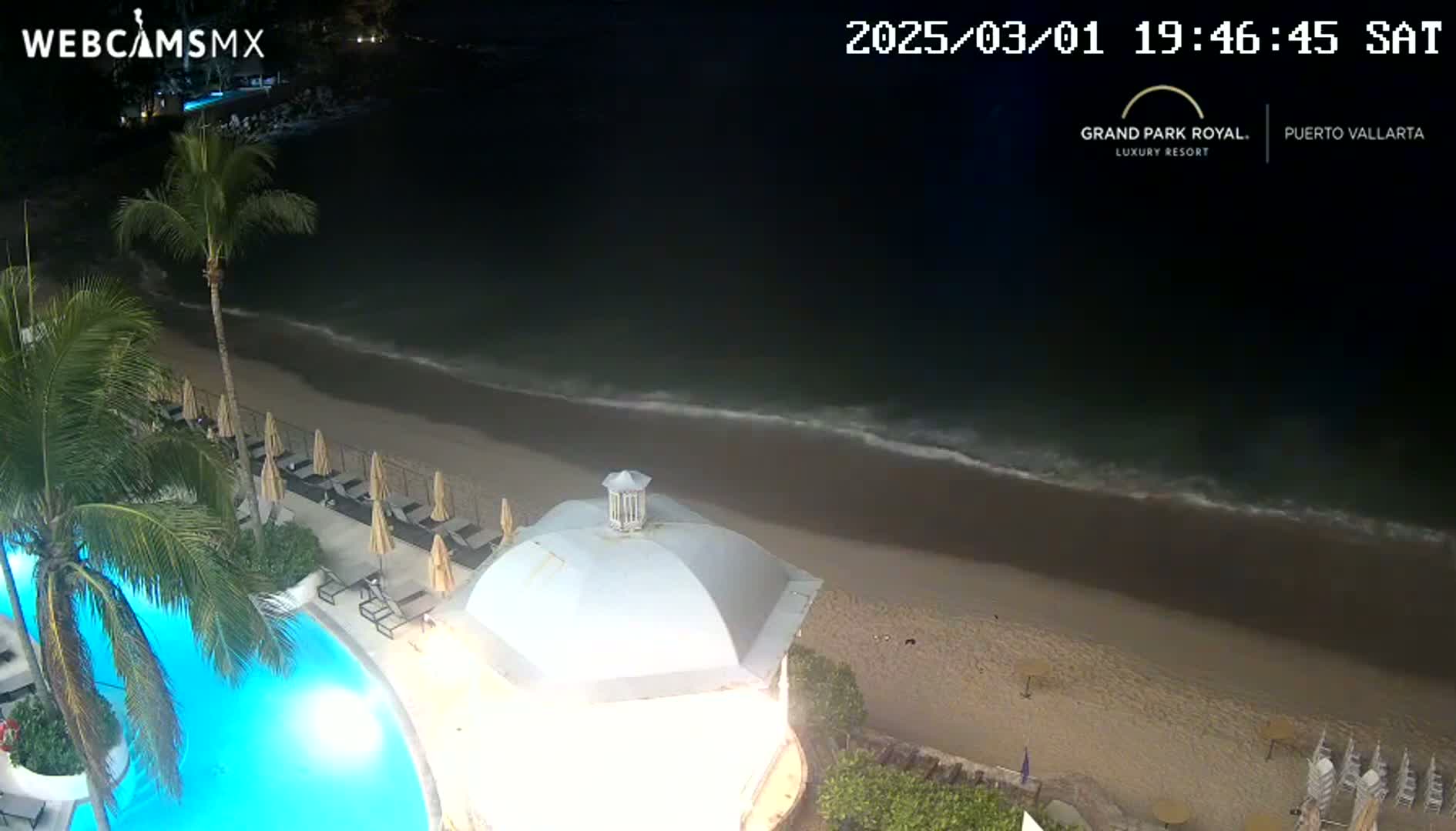 A nighttime view of a resort pool and beach, with calm ocean waves lapping the shore.
