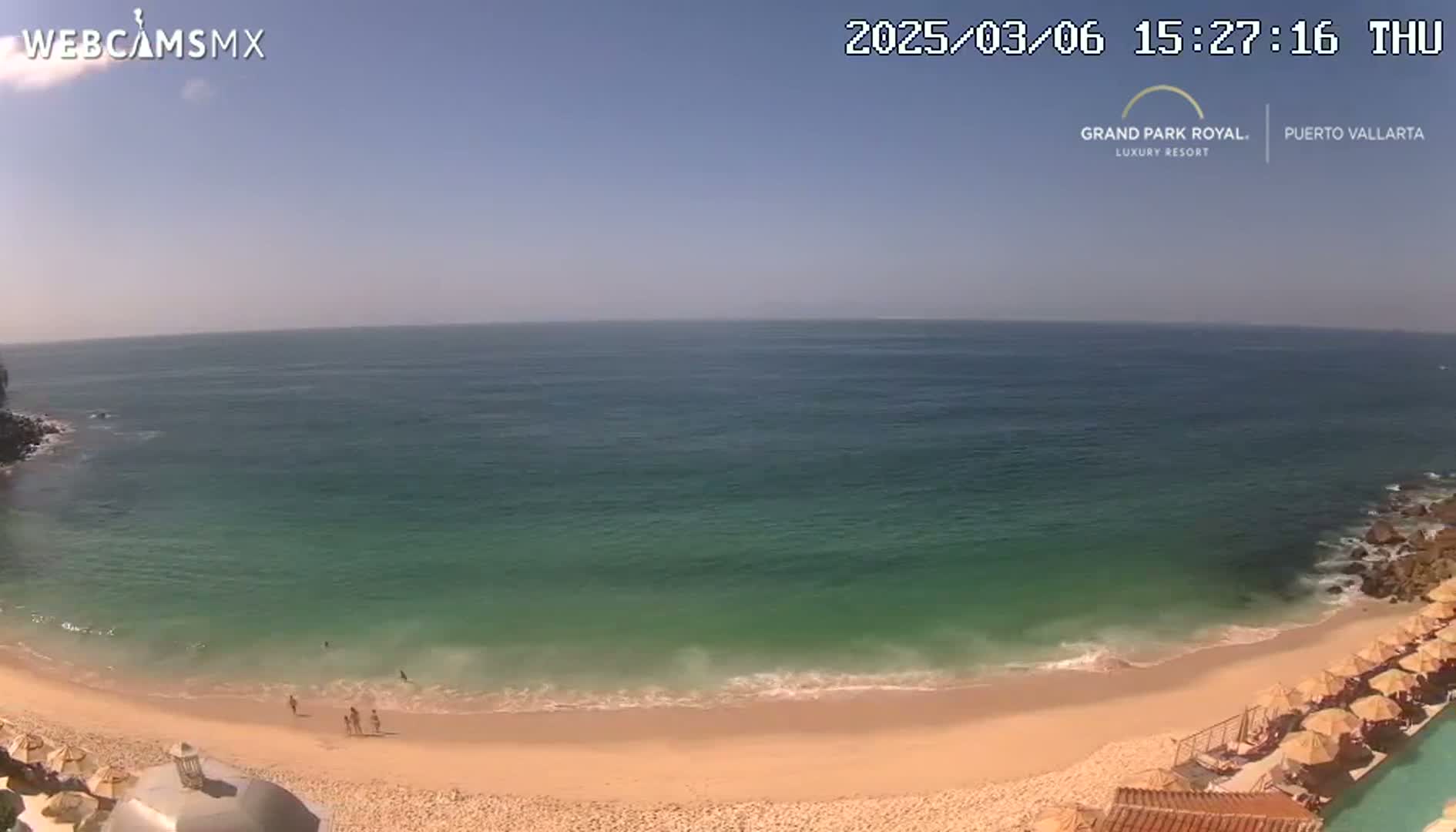 A sandy beach with calm, teal-colored water under a clear, sunny sky.