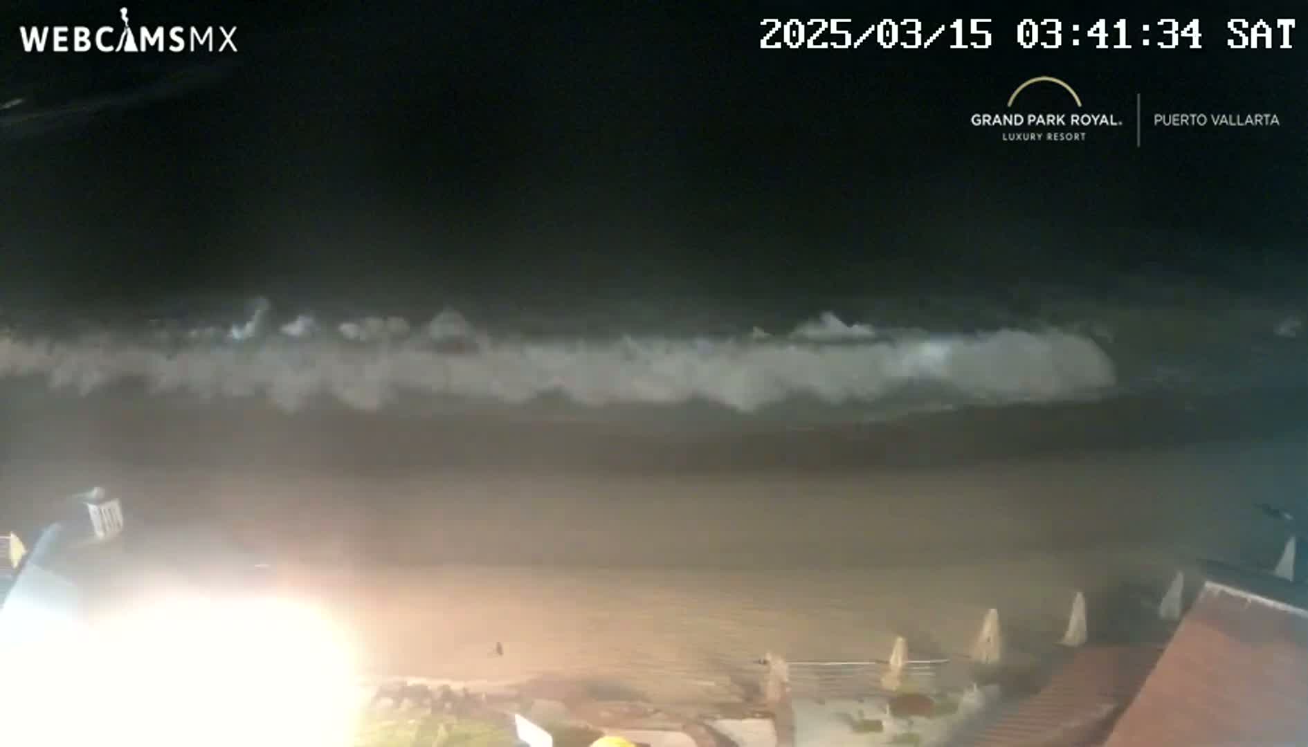 A nighttime beach scene shows a line of waves breaking on the shore under a dark sky.