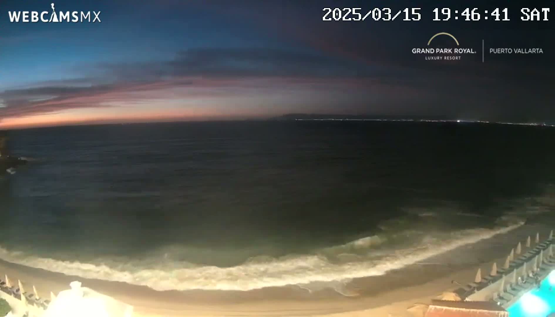 A dark ocean with waves rolling onto a sandy beach under a twilight sky.