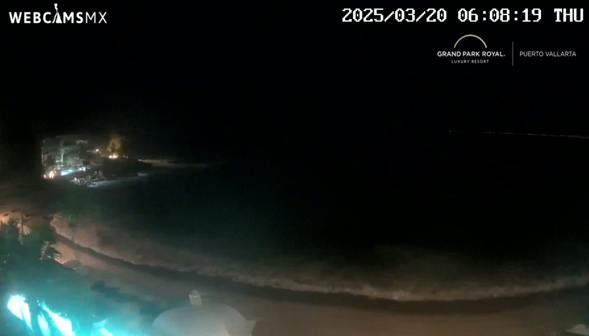 A nighttime view of a dark beach with gently lapping waves under a clear sky.