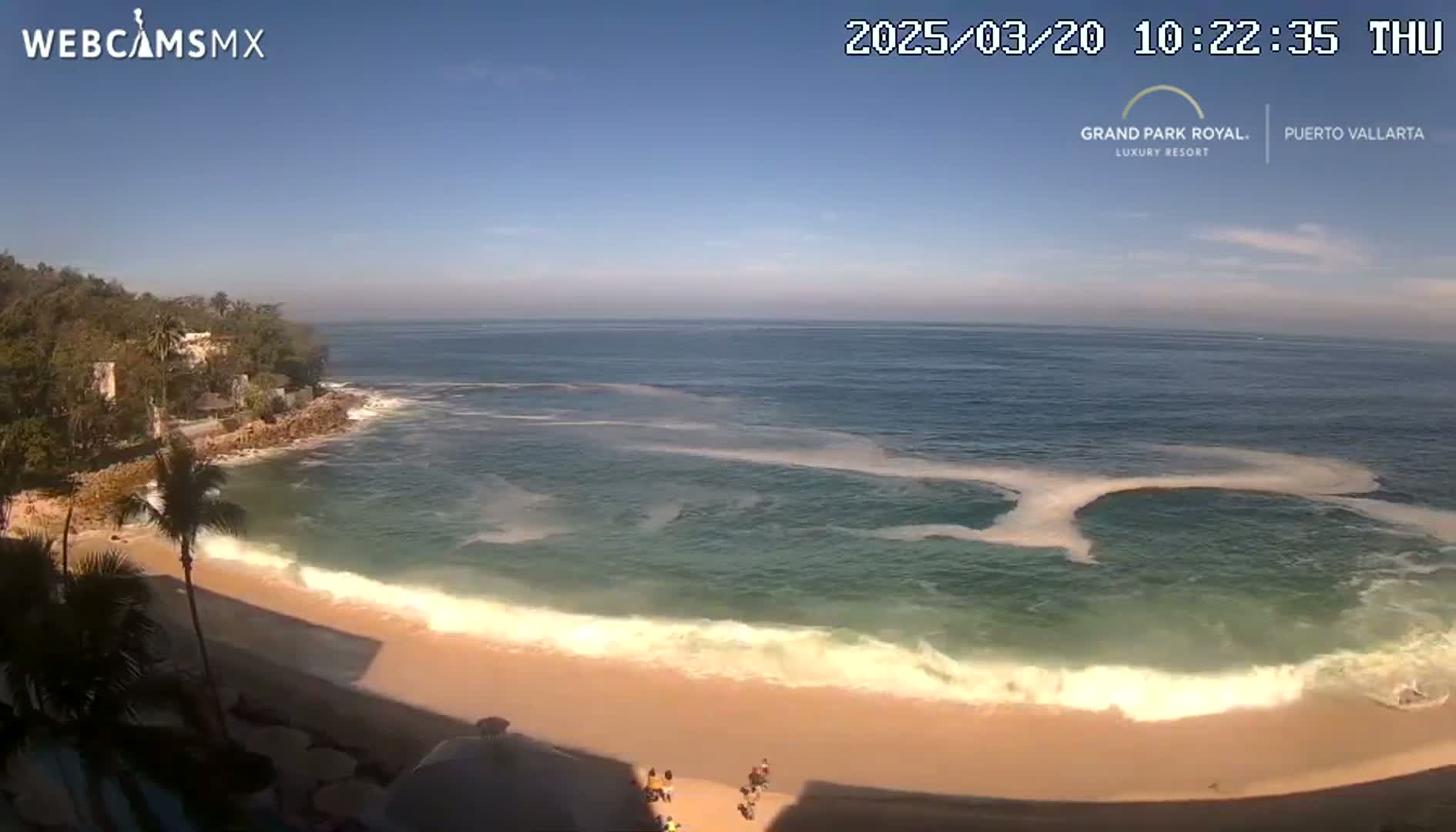 A sandy beach with gentle waves meets a calm ocean under a clear blue sky.