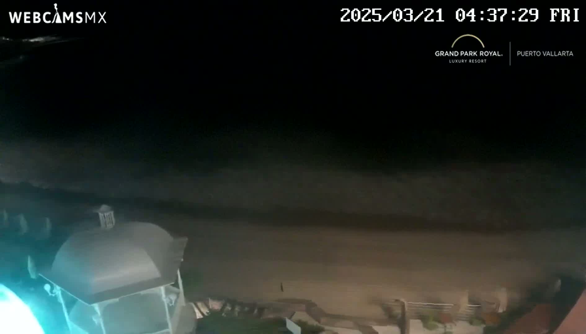 A nighttime view of a dark beach with calm waves, seen from an elevated vantage point overlooking a structure with a gabled roof.