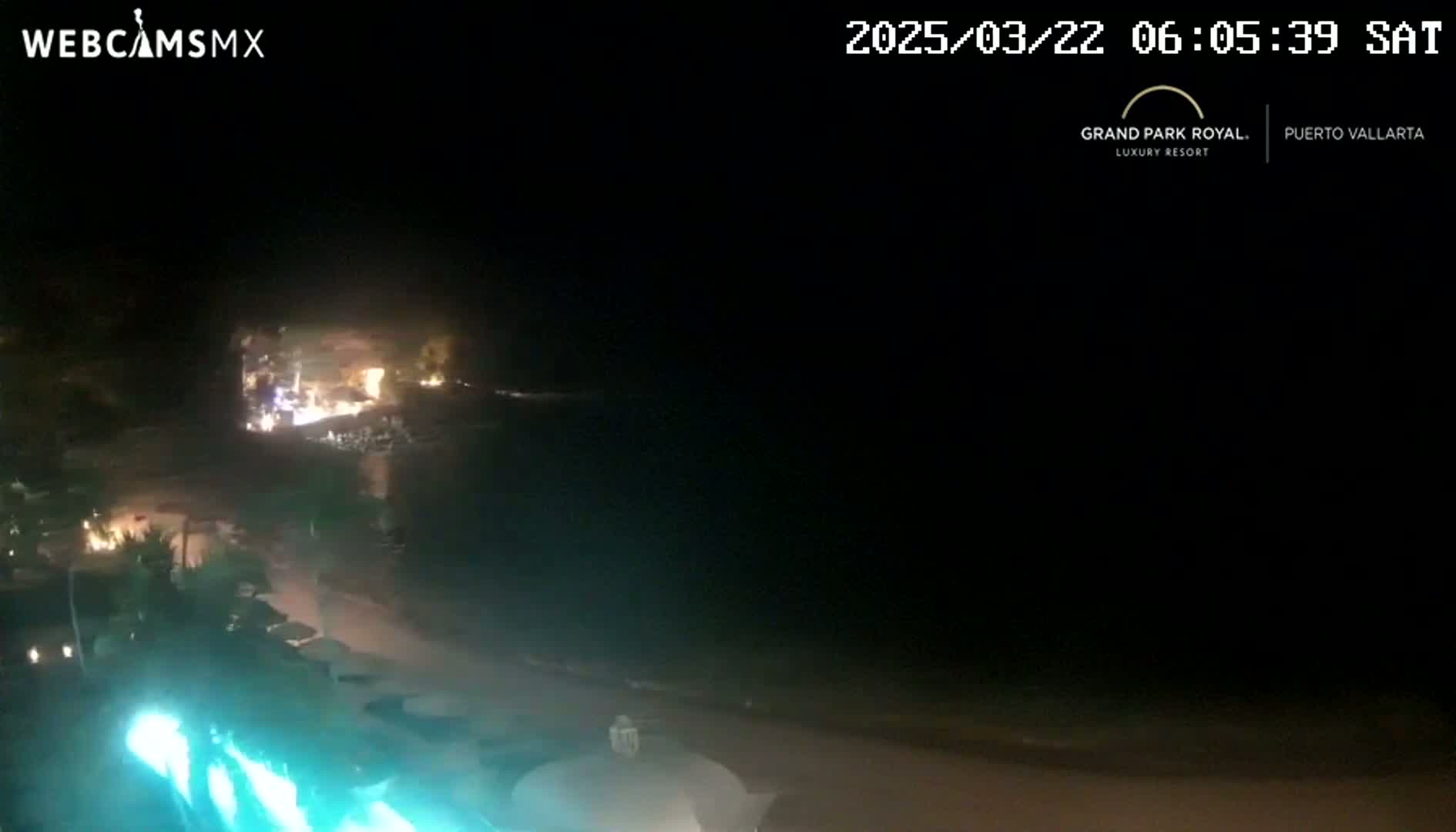 A nighttime view of a beach with lights visible on the shore and in the water, under a clear, dark sky.