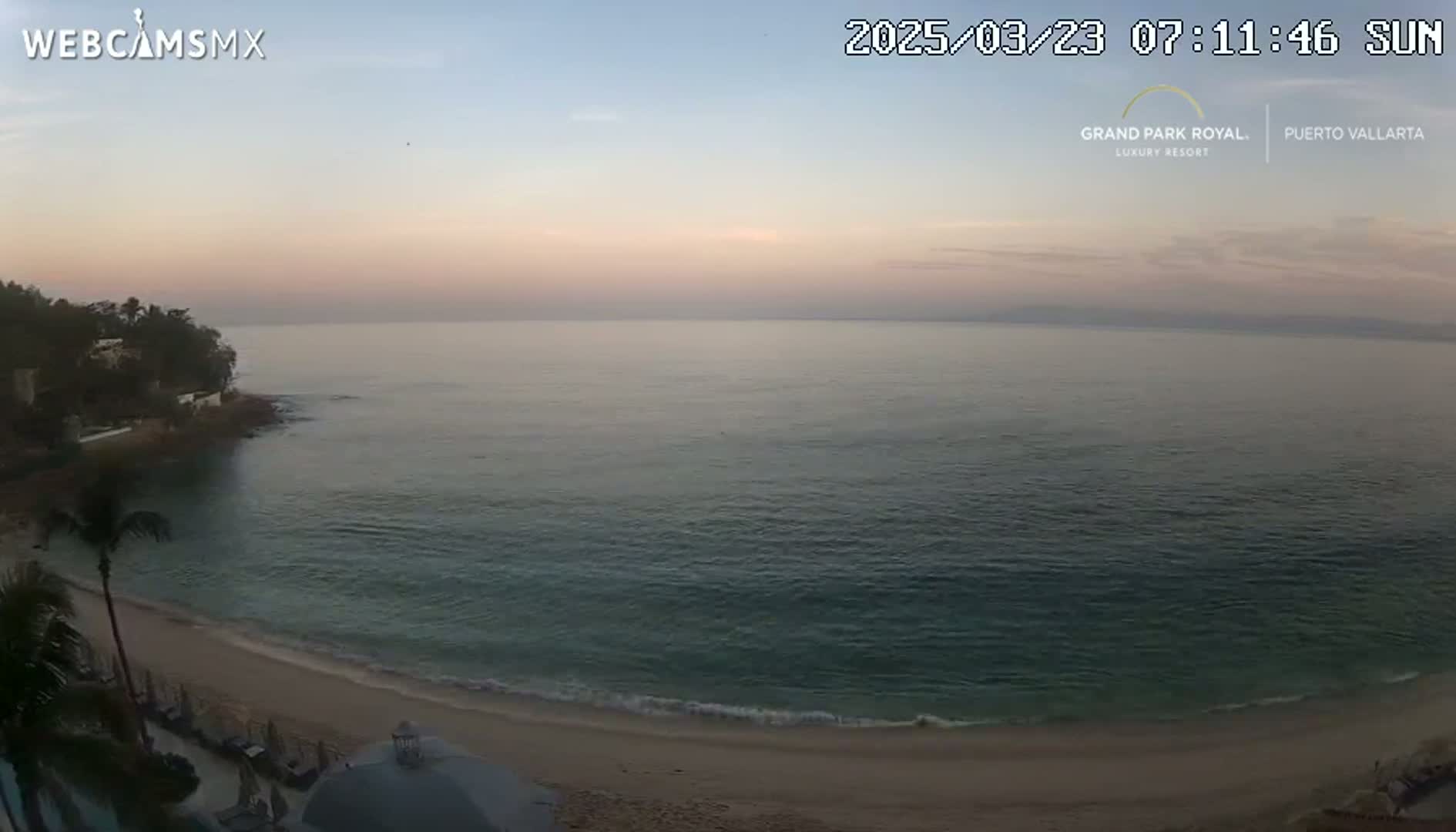A sandy beach and calm ocean are visible at sunrise, with a rocky shoreline and vegetation in the background.