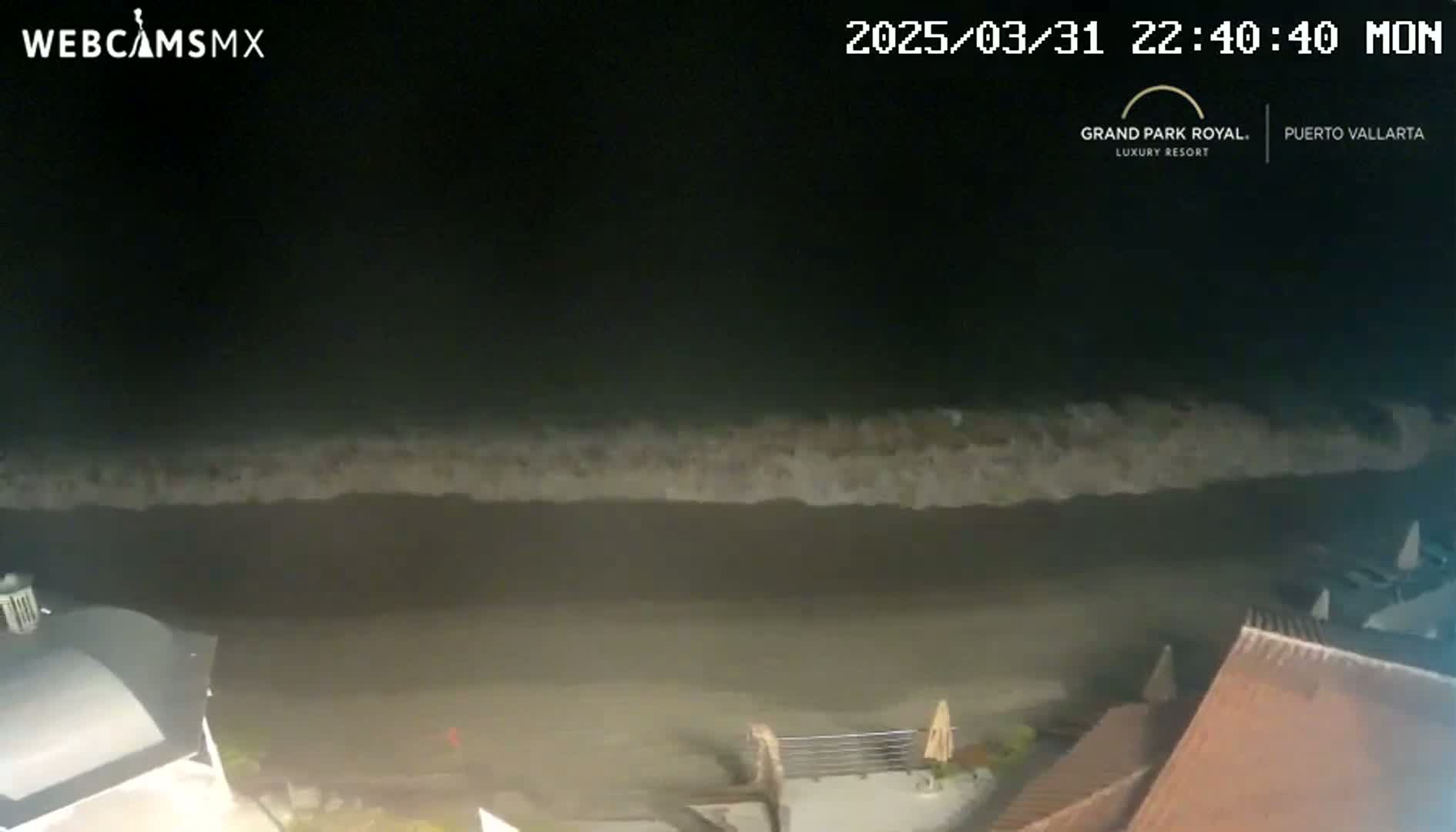 A nighttime view of dark ocean waves lapping a shore near a building.