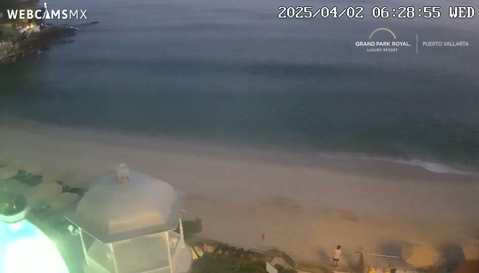 An elevated view shows a sandy beach and calm ocean at dusk, with a small structure partially visible in the foreground.