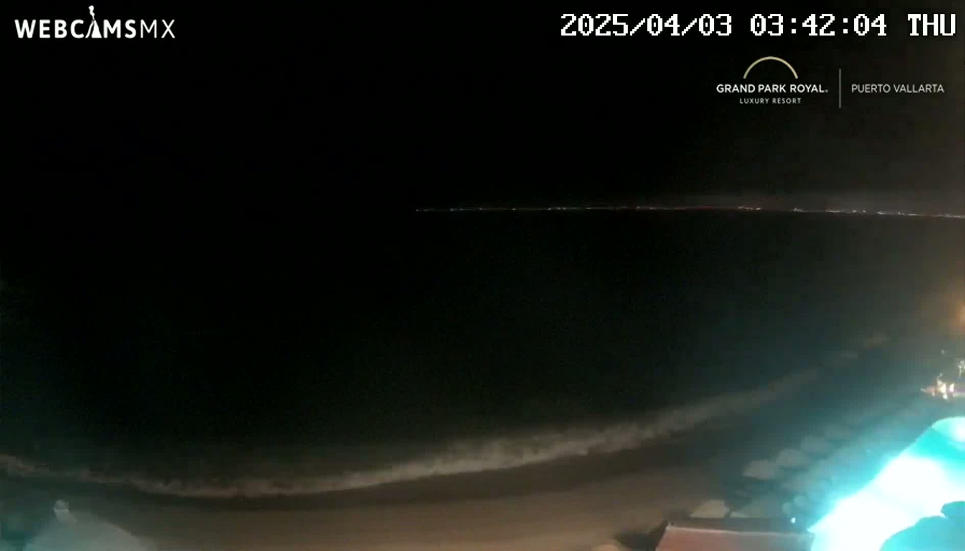 A dark nighttime beach scene shows gently lapping waves on a sandy shore under a clear, starless sky.