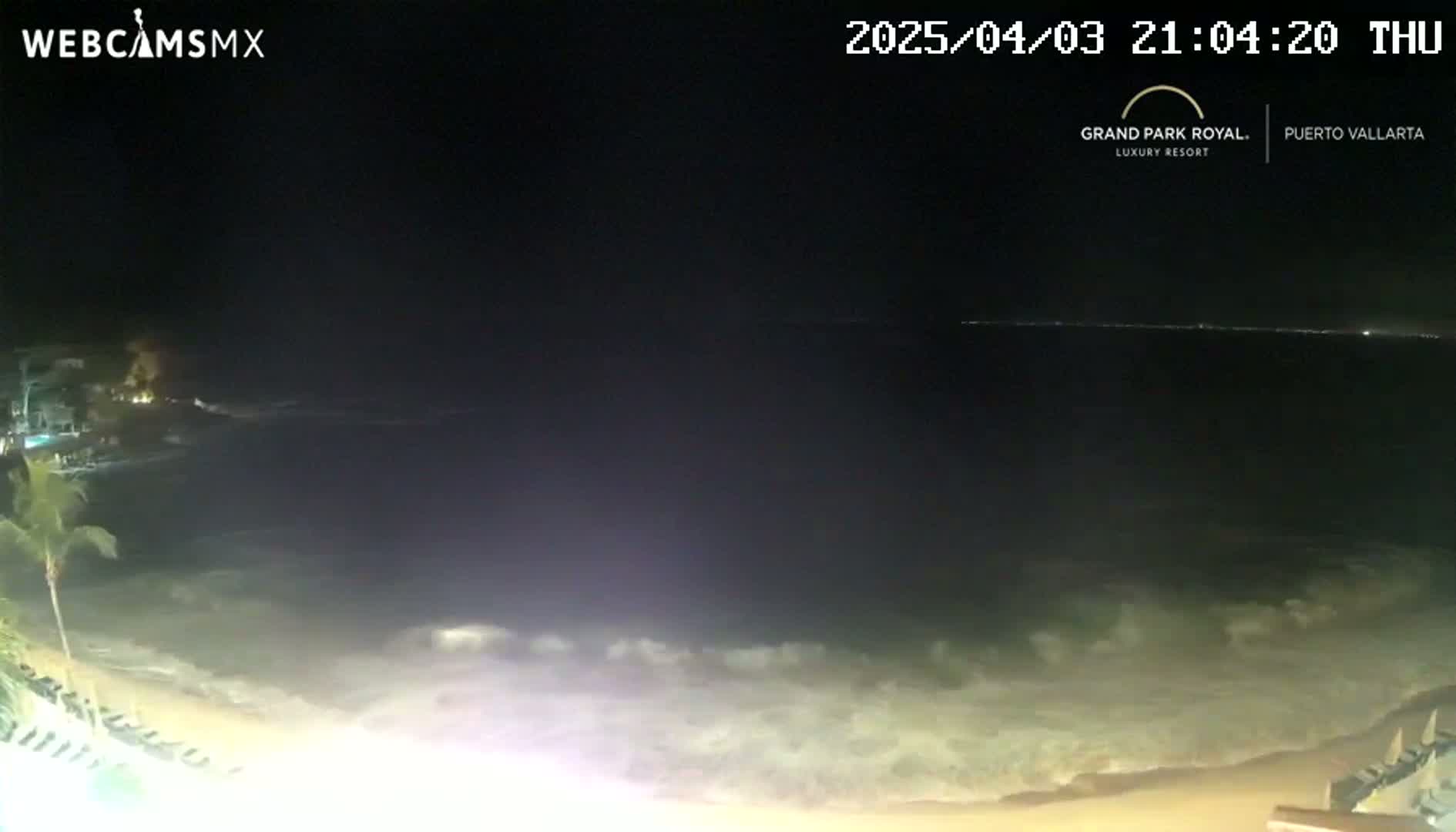 A nighttime beach scene shows gentle waves lapping the shore under a dark sky.
