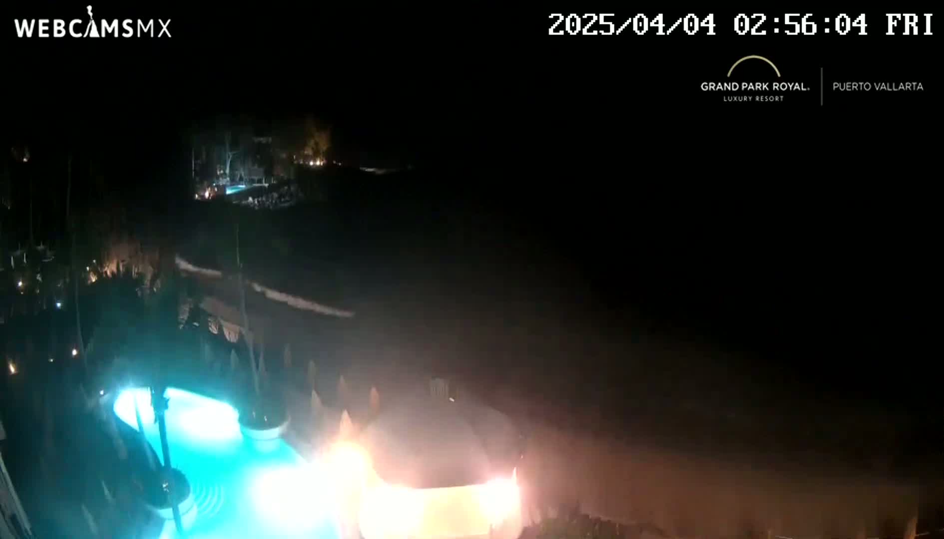 A nighttime view shows a brightly lit swimming pool and a dark ocean under a clear, moonless sky.