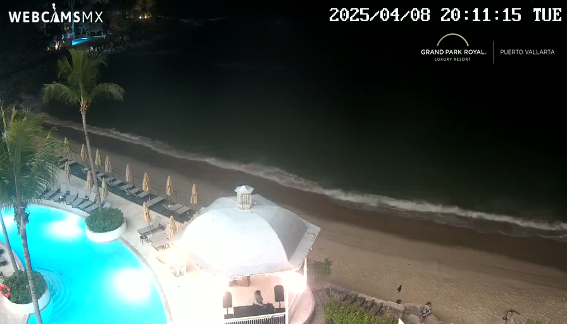 An illuminated pool and beach at night, with gentle waves lapping the shore.