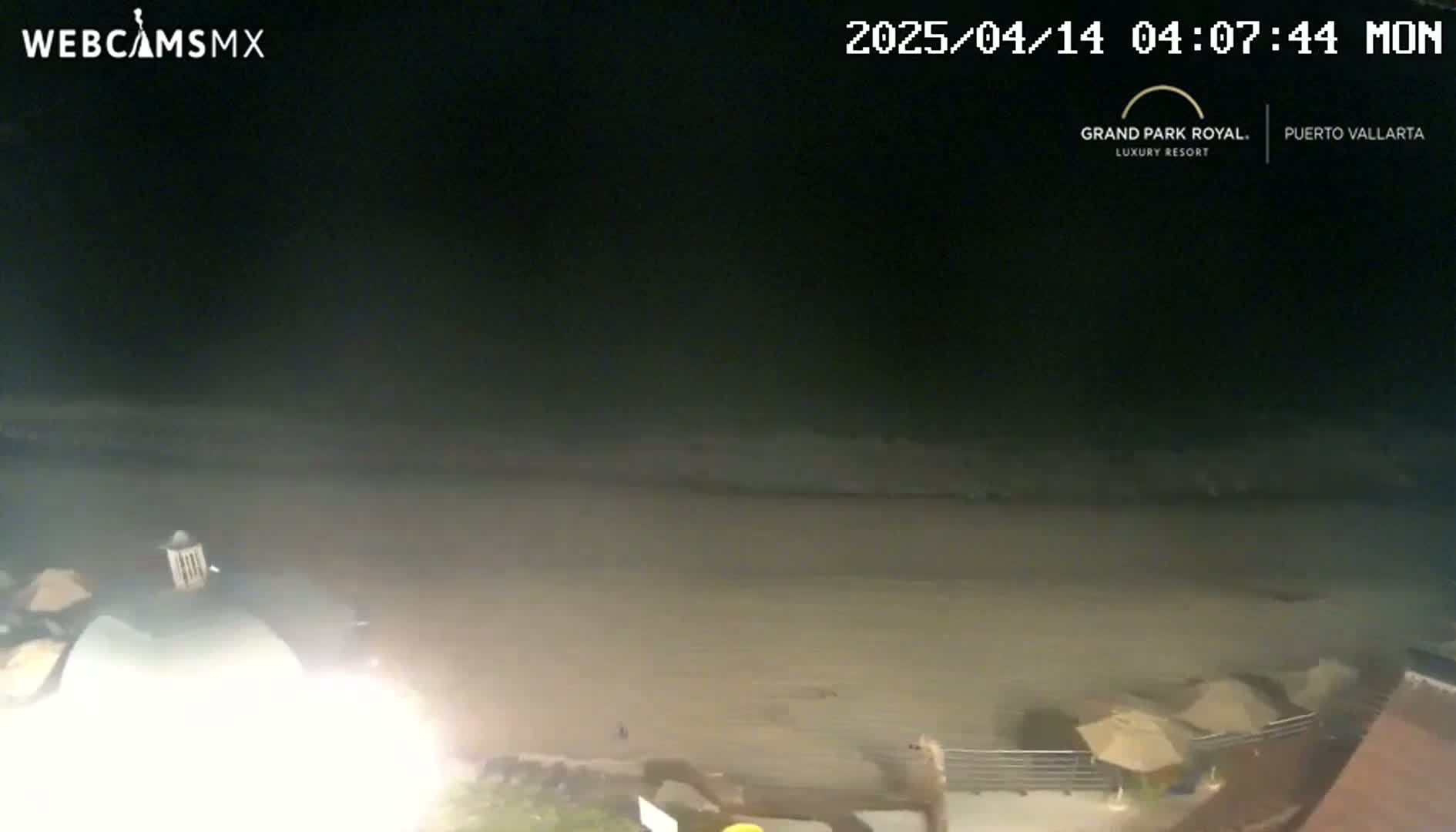 A nighttime beach scene shows dark water lapping a light-colored sandy shore, with some beach umbrellas visible in the lower right corner.