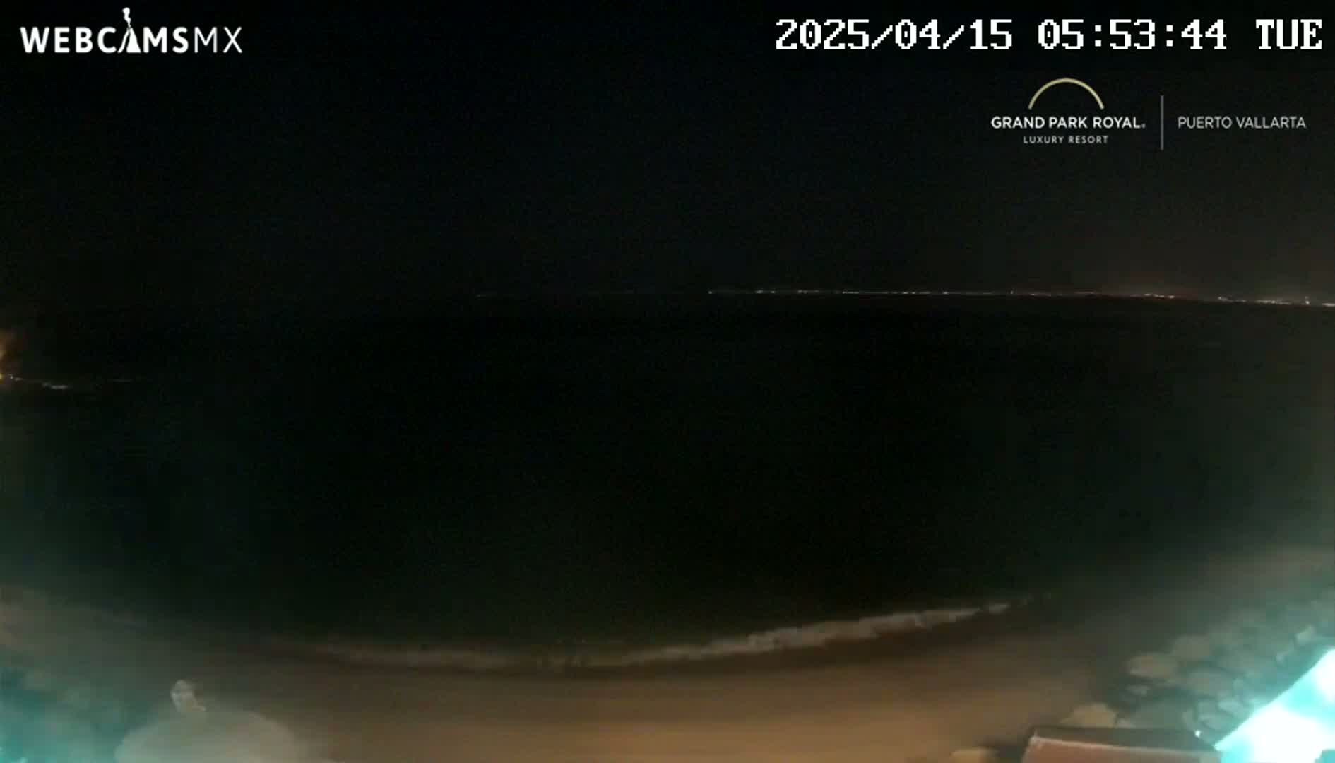 A nighttime beach scene shows a dark ocean with a faint line of lights on the horizon, and a dark sandy shoreline.