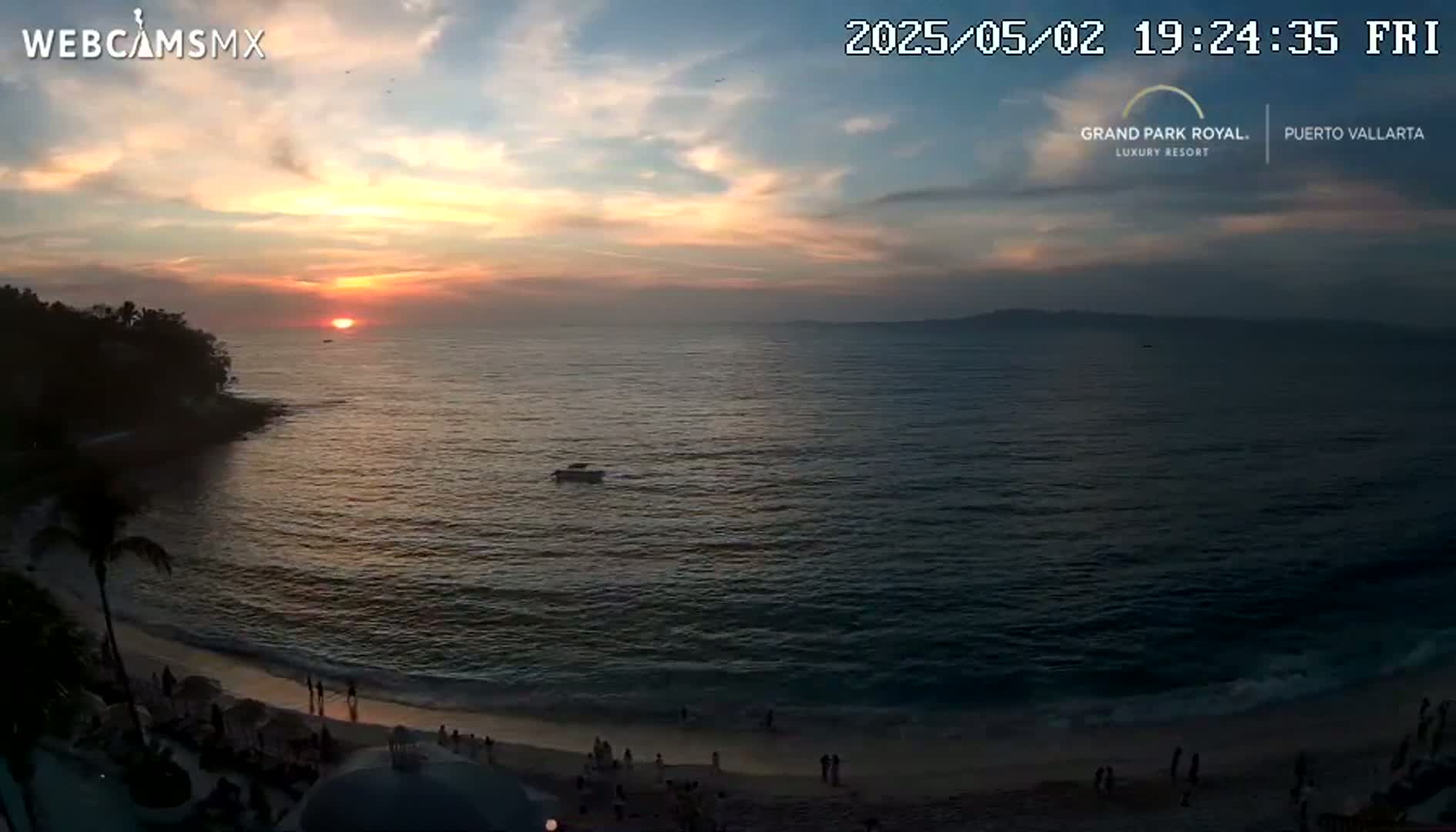 A sunset over a calm ocean beach with a few people on the sand.