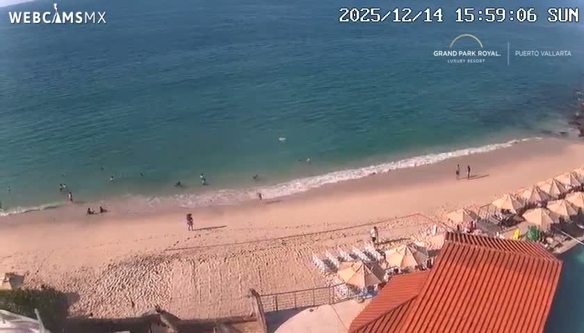 The image shows a clear night view overlooking a body of water with a distant city skyline illuminated across the horizon, while a brightly lit swimming pool and beach chairs are visible in the foreground.