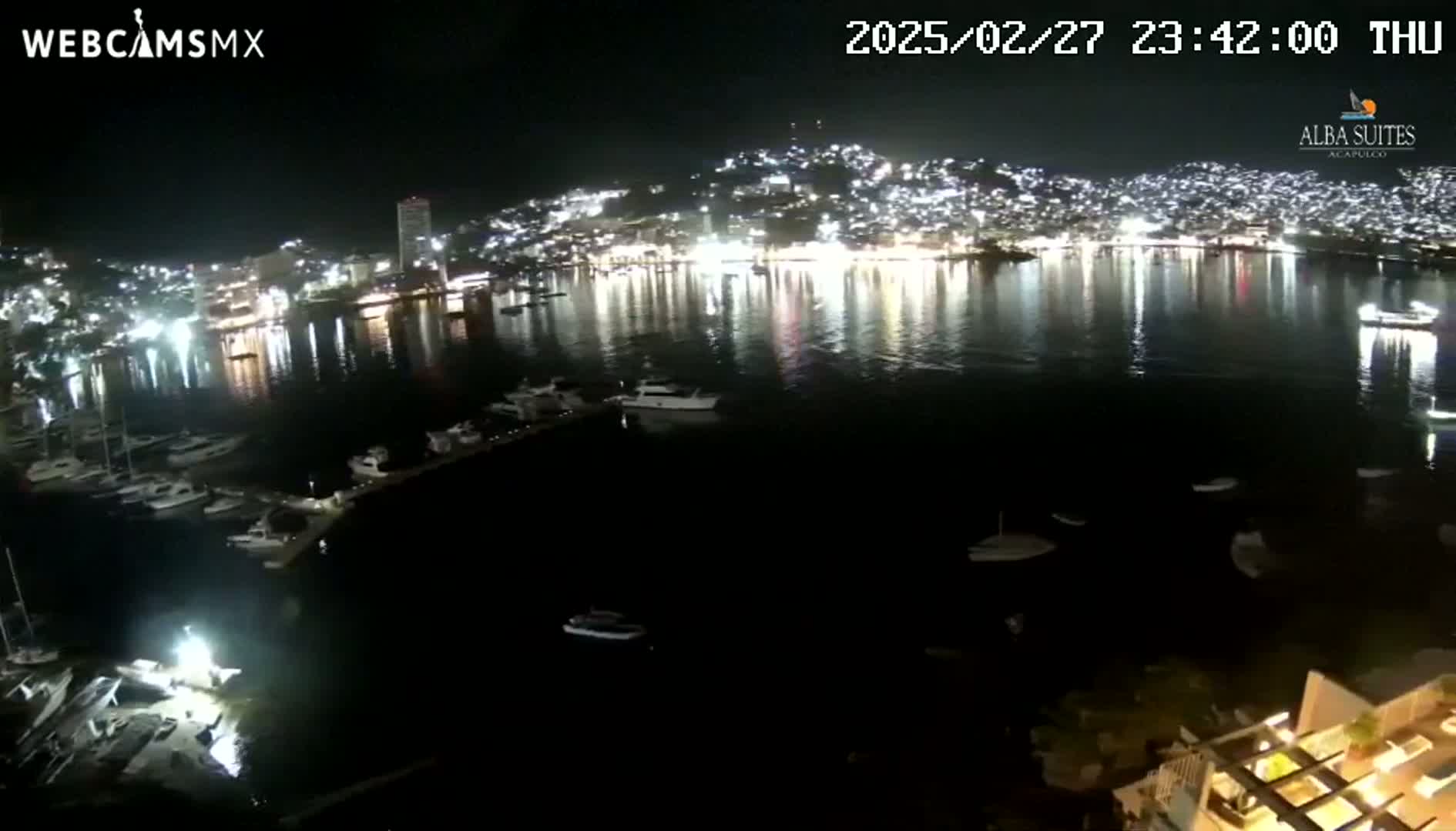 A nighttime view of a brightly lit city across a dark body of water dotted with boats and yachts.
