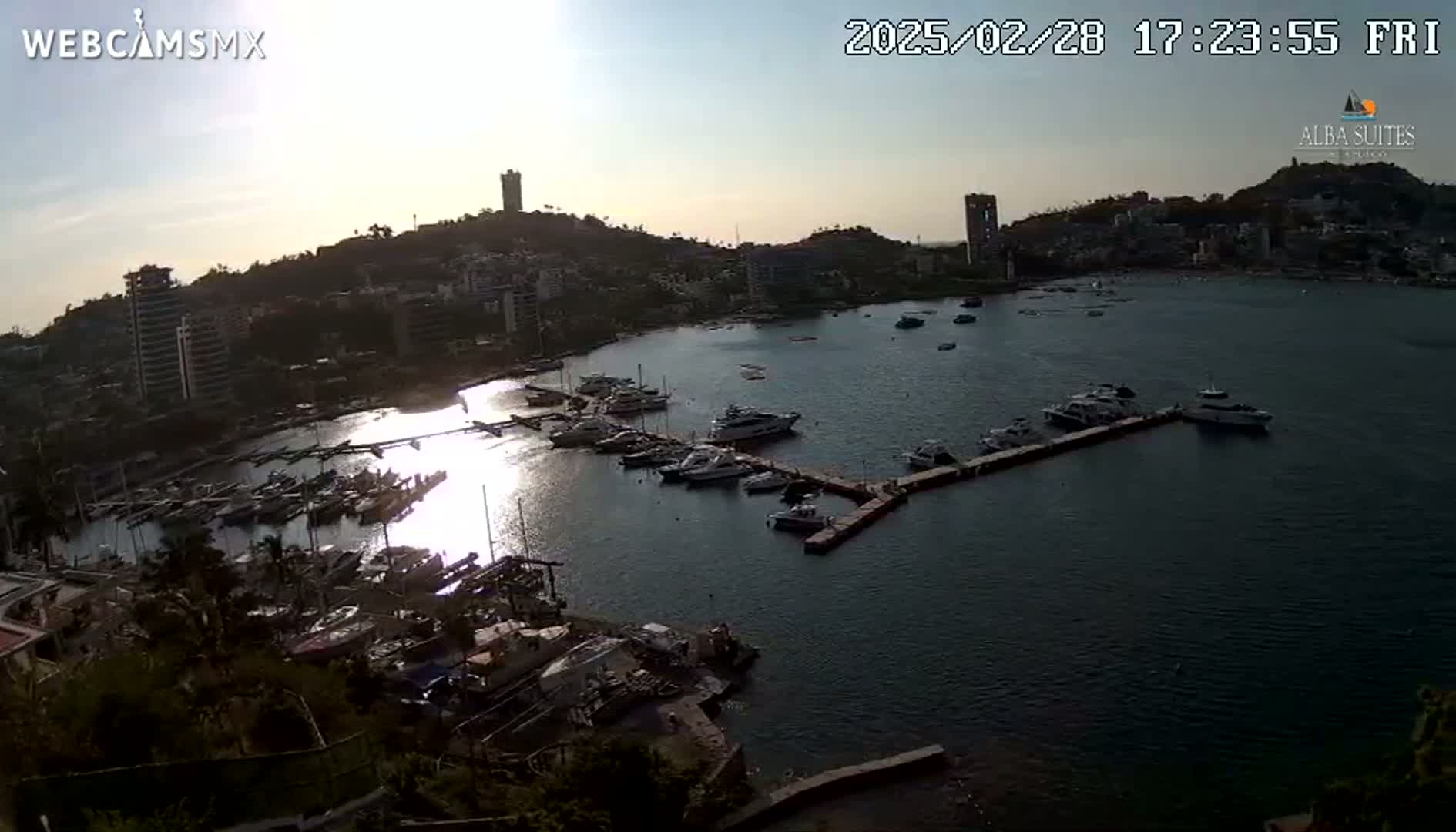 A marina filled with boats is nestled in a bay near a city under a partly sunny sky.