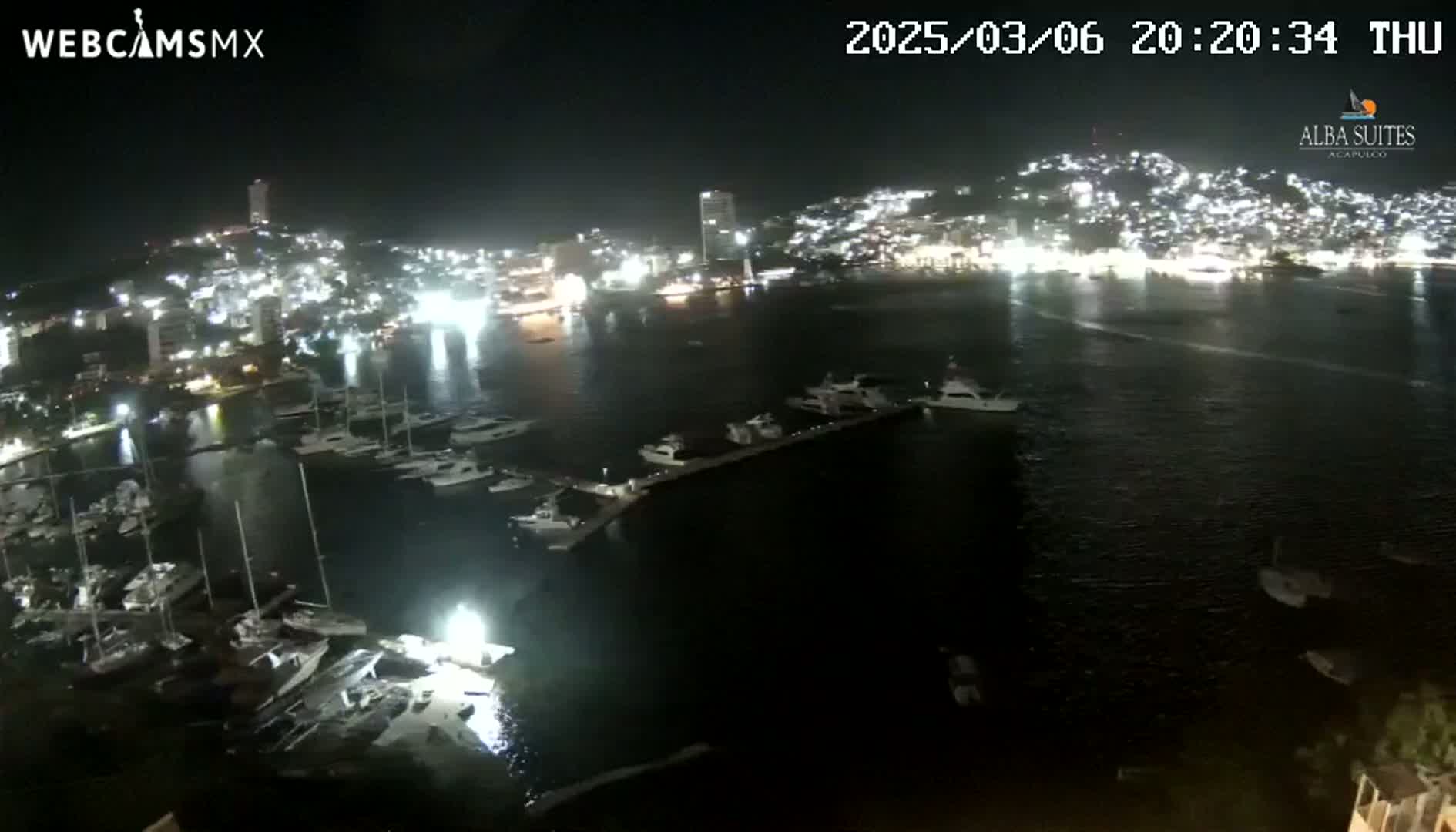 A nighttime view of a harbor filled with boats, adjacent to a brightly lit city on a hill.