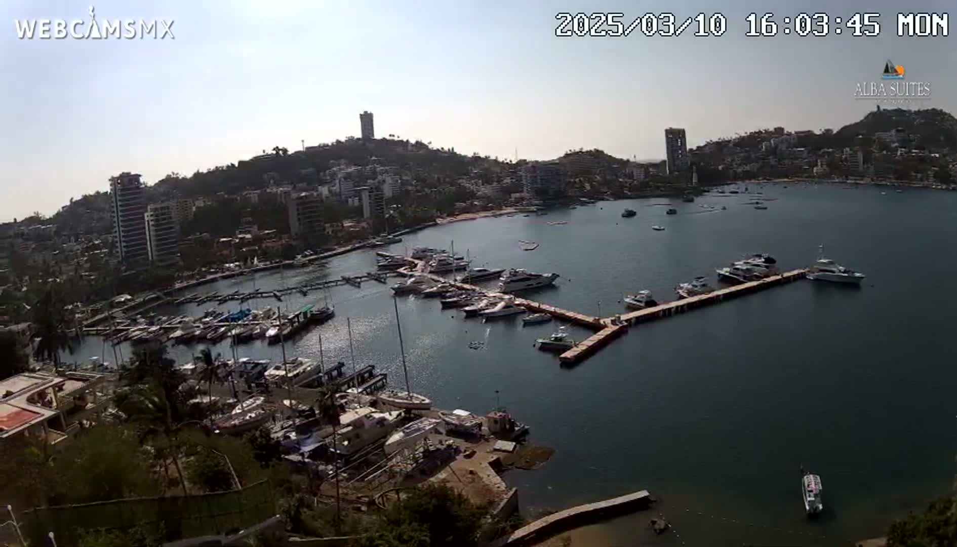 A sunny day overlooking a marina filled with numerous boats and yachts, situated in a coastal town with buildings nestled on a hillside.