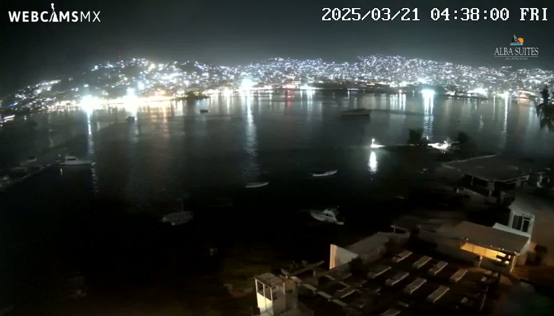 A nighttime view of a city illuminated along a dark bay with several boats visible on the water.
