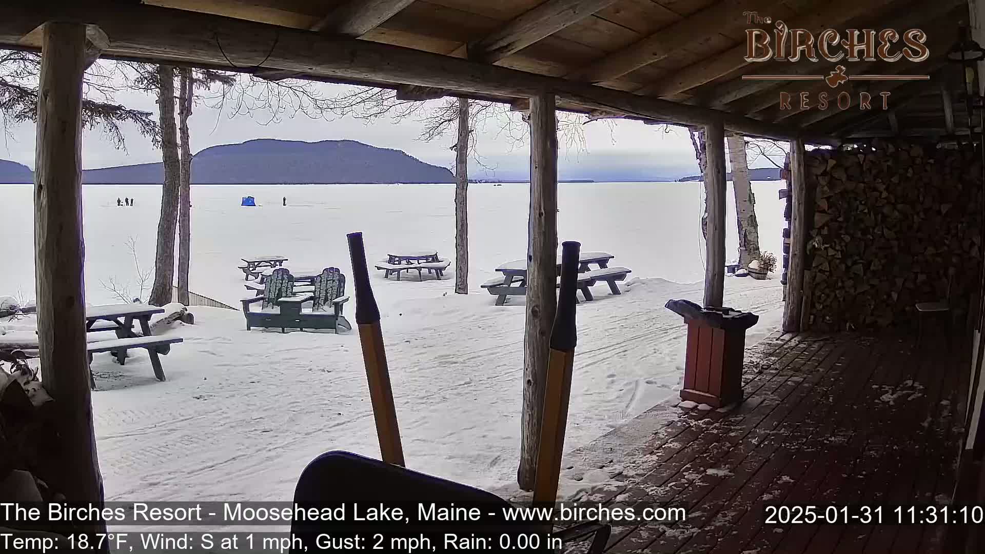 A snow-covered porch overlooks a frozen lake with mountains in the distance under an overcast sky.