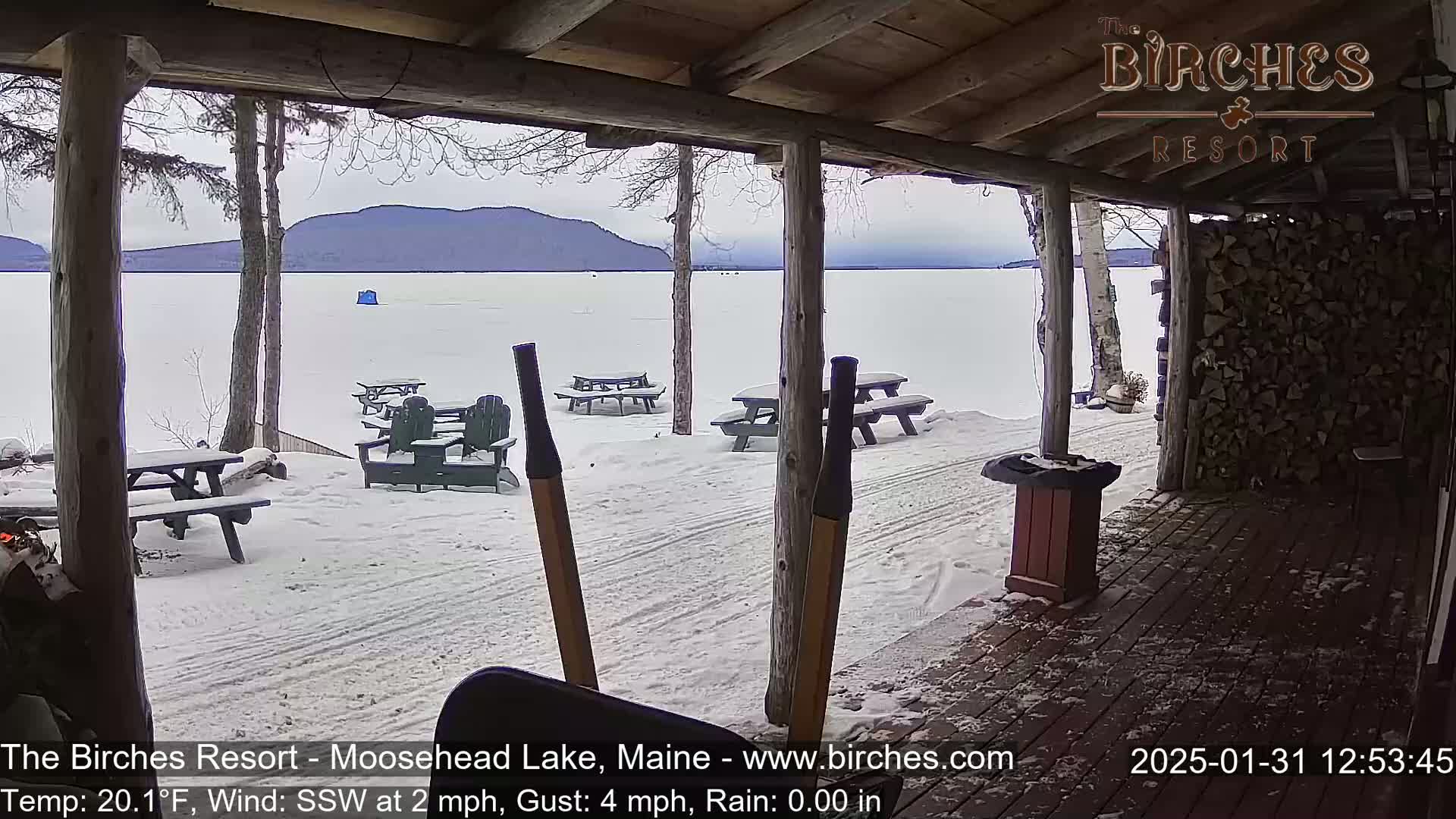A snow-covered porch overlooks a frozen lake with distant mountains under an overcast sky.