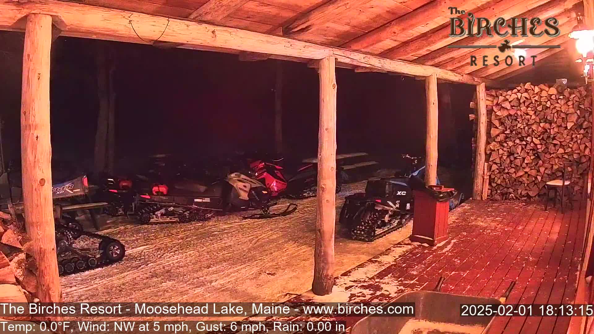 Several snowmobiles are parked under a covered wooden porch during a nighttime rainstorm.