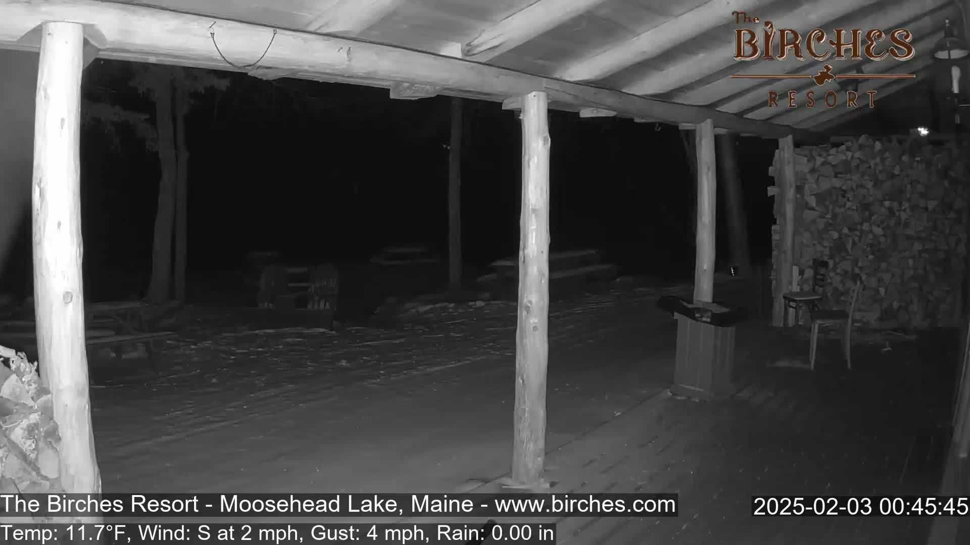 A snow-covered porch with wooden posts and a woodpile is visible at night under a dark sky.