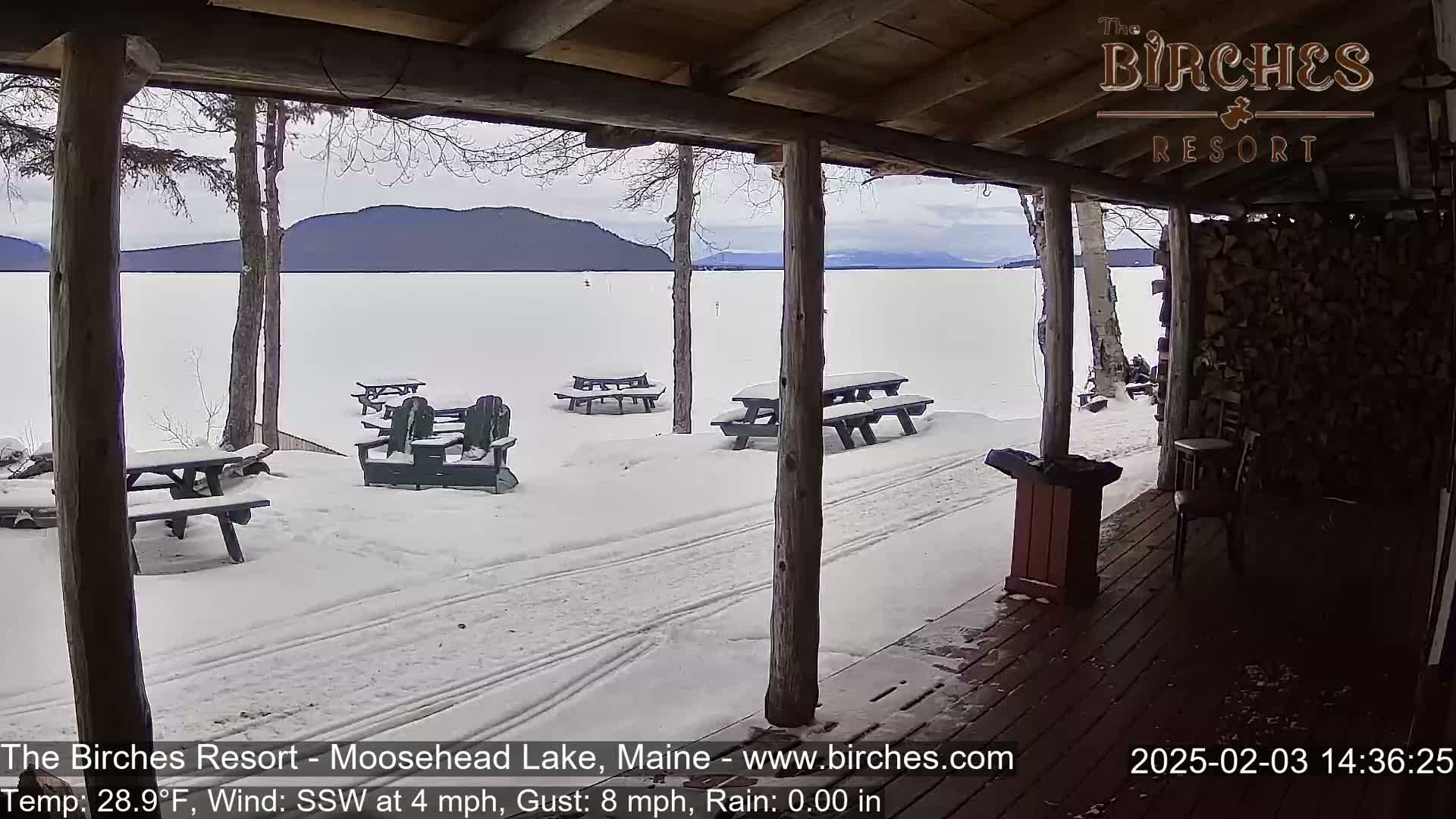 A snow-covered porch overlooks a frozen lake and distant mountains under a cloudy sky.