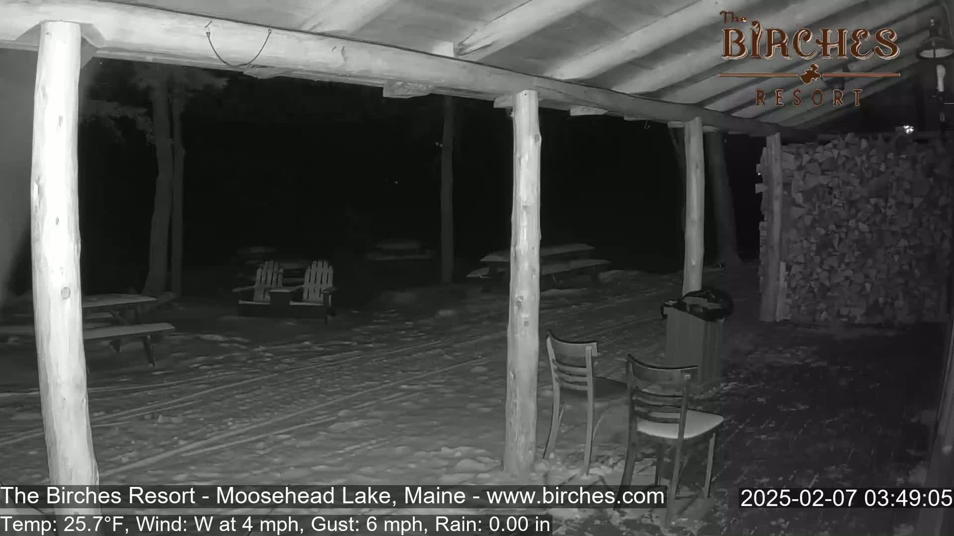 A snow-covered outdoor patio with picnic tables and chairs is visible at night under a covered porch, with a 4 mph westerly wind and gusts up to 6 mph.