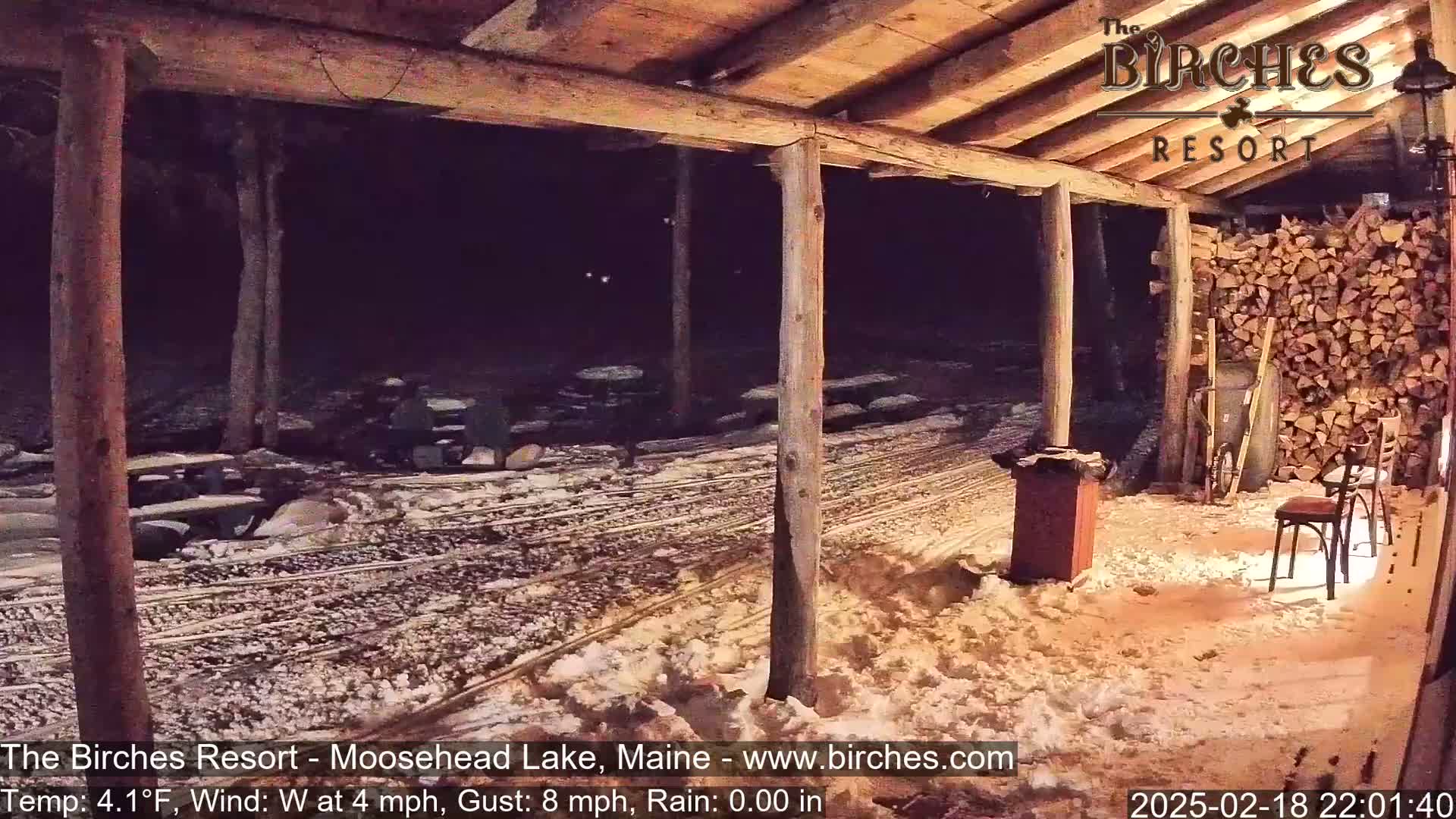 A snow-covered area outside a wooden structure at night, viewed from under a covered porch.