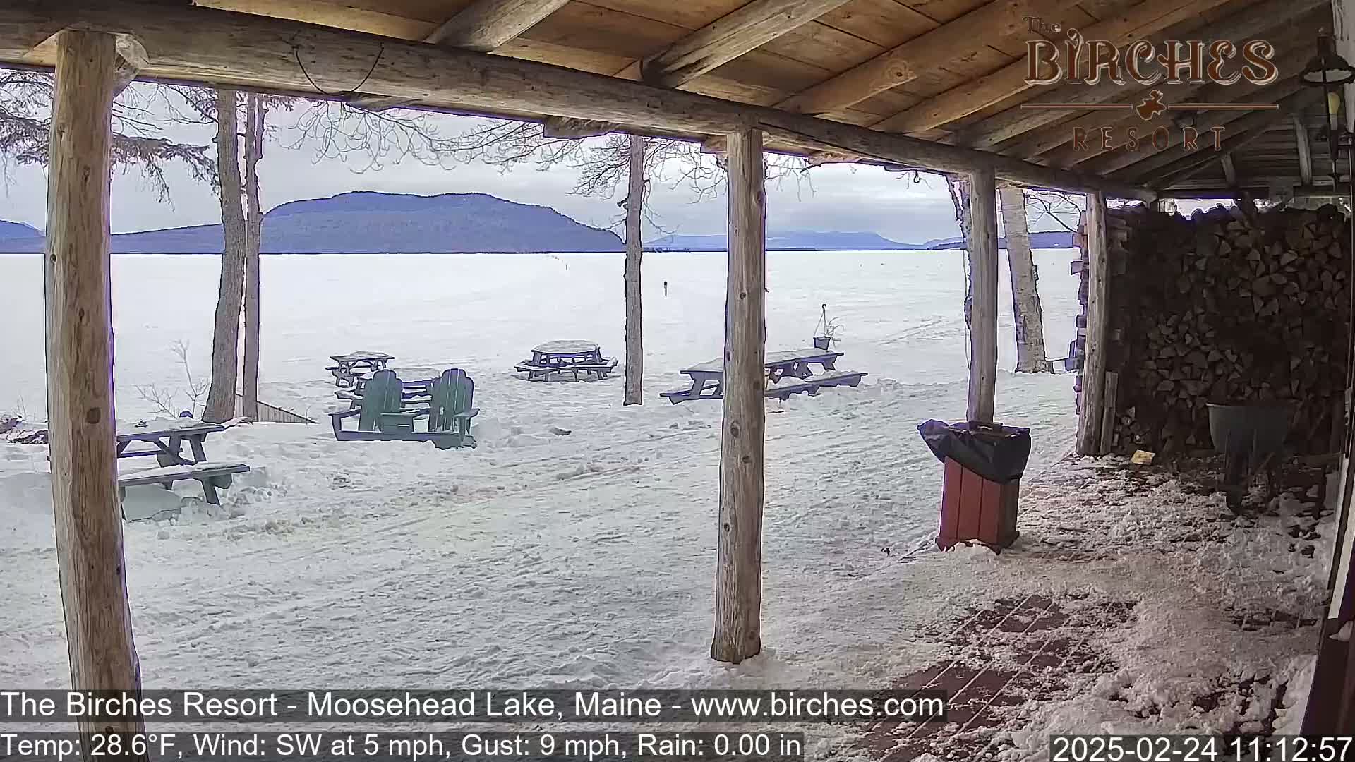 A snow-covered porch overlooks a frozen lake and distant mountains under a cloudy sky.