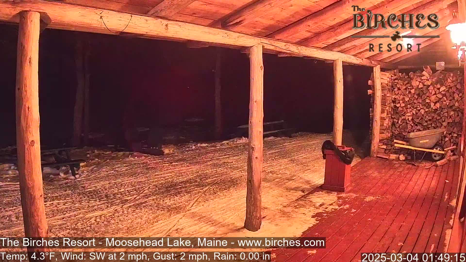 A snow-covered outdoor area with wooden posts and a red deck is visible at night, under a southwest wind.
