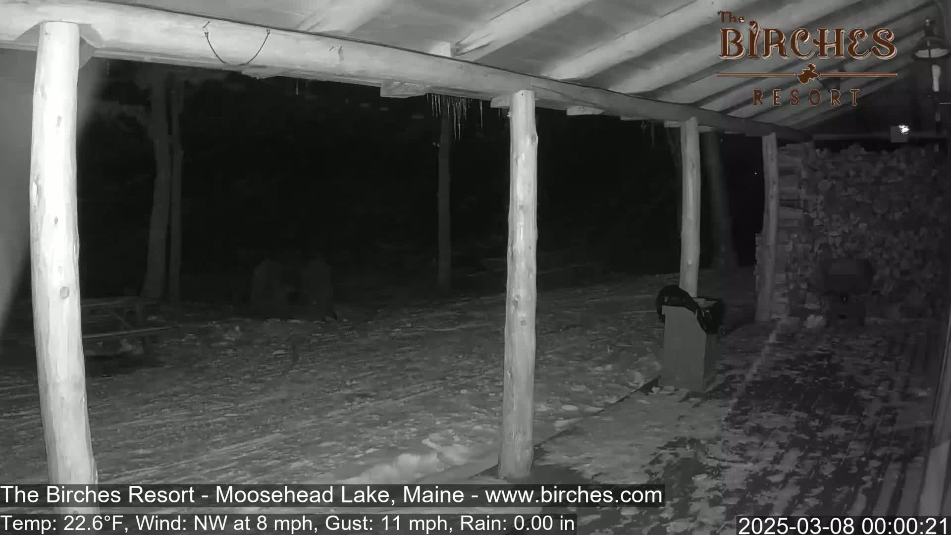 A snow-covered porch area with wooden posts and icicles hanging from the roof is visible at night under a northwest wind.