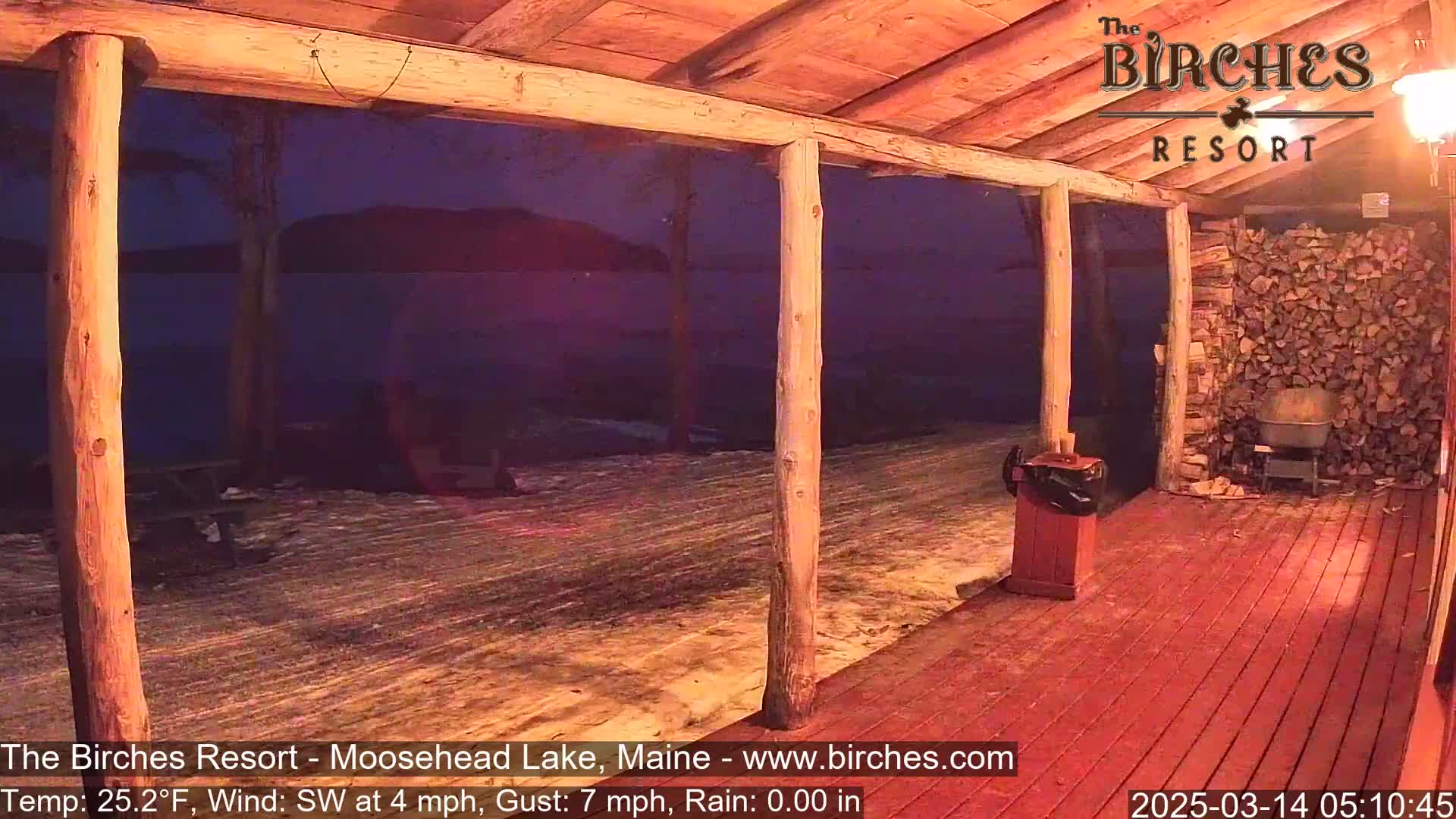 A snow-covered porch with wooden posts overlooks a dark lake under a night sky, with a southwest wind at 4 mph and gusts up to 7 mph.