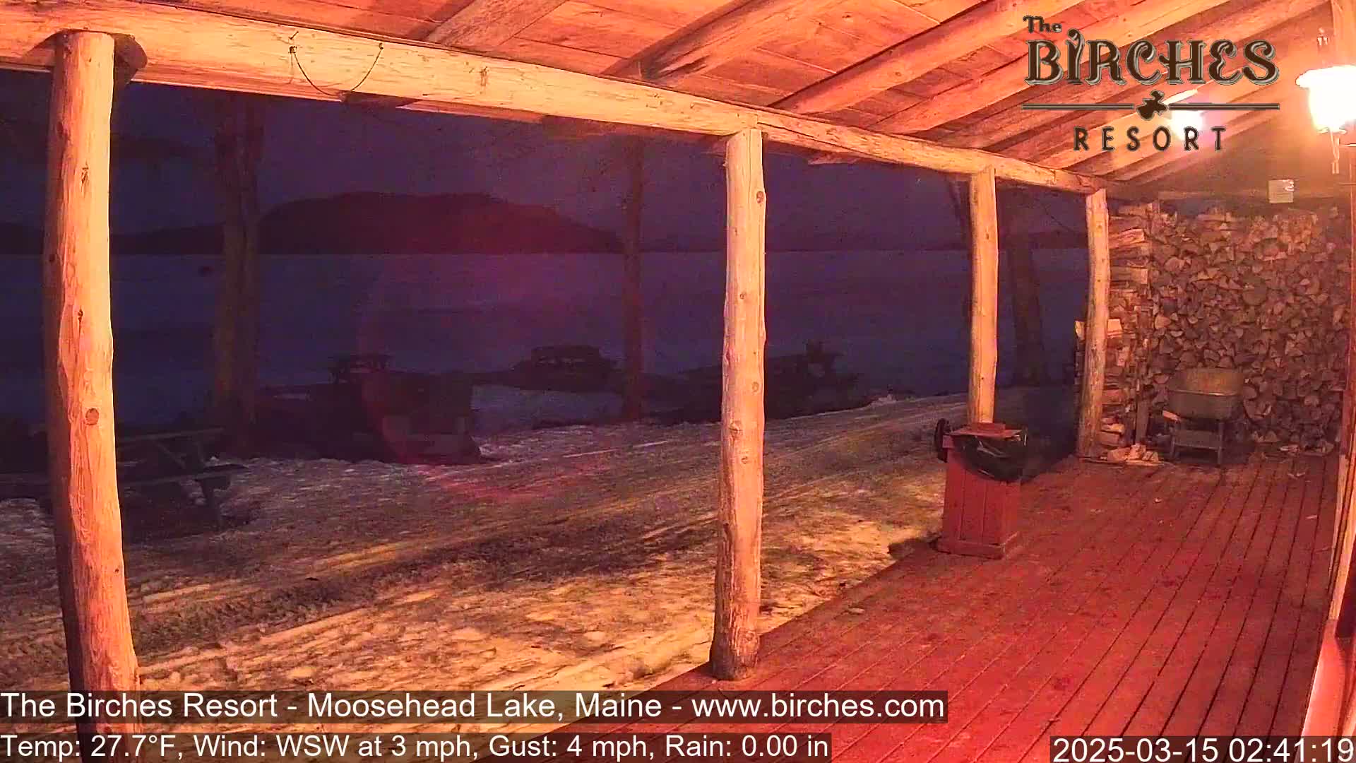A nighttime view from a wooden porch shows a dark lake and snow-covered ground under a clear sky.