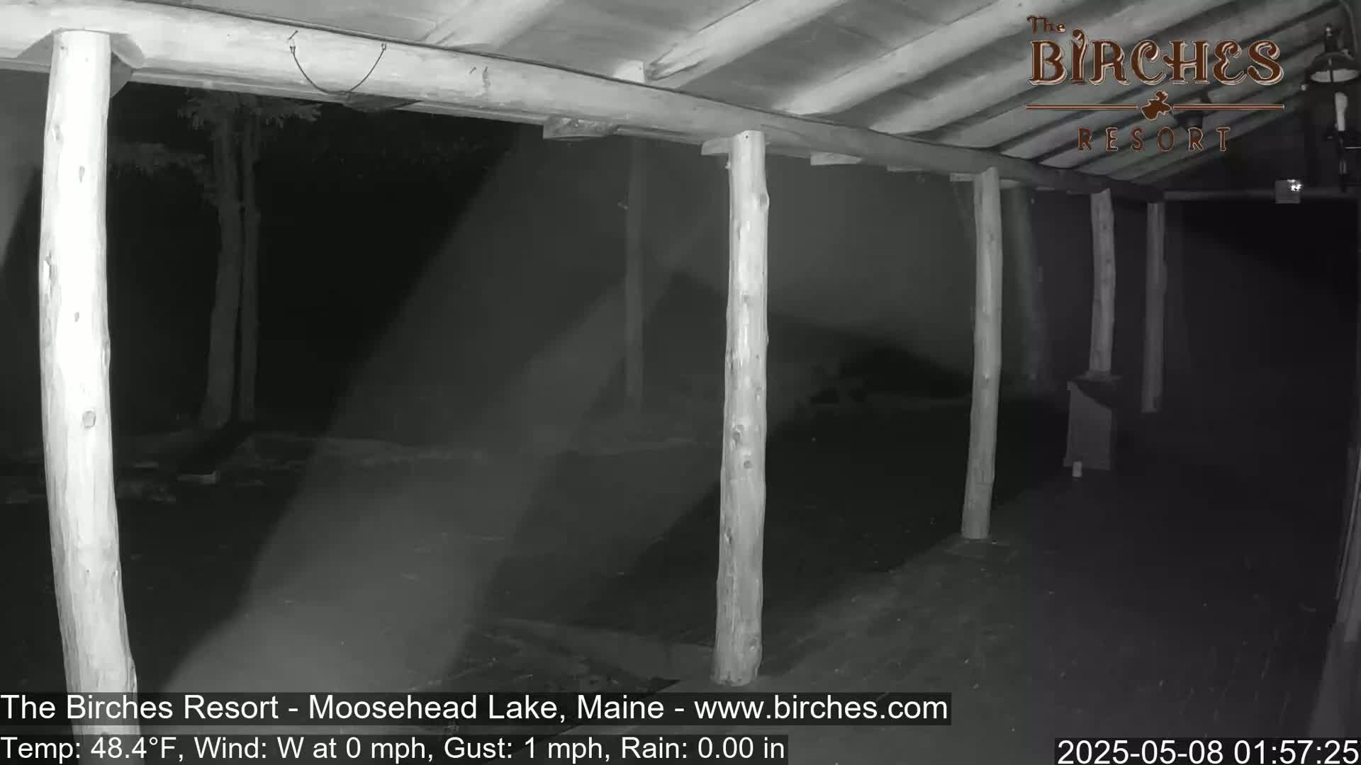 A nighttime, low-light view of a covered porch area with wooden posts and a dark, rainy background.