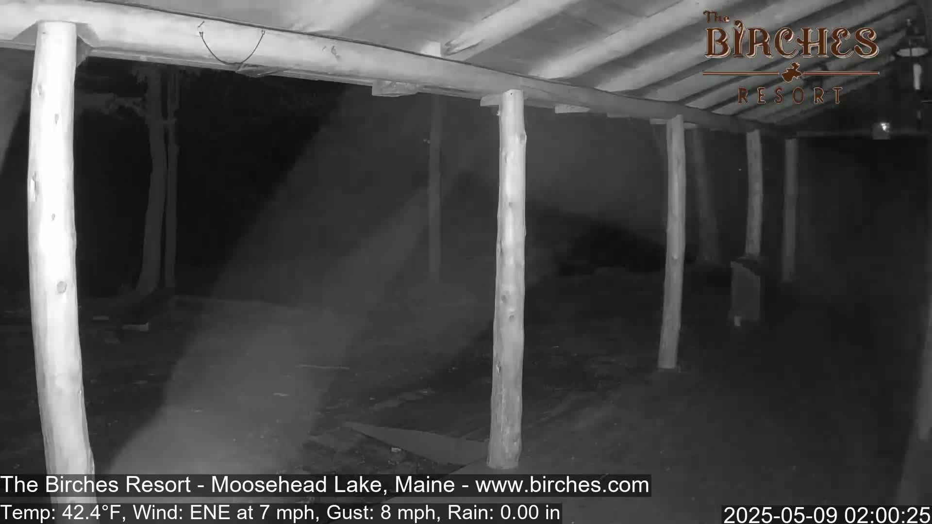 A dark, open-air structure with wooden posts is seen at night in rainy weather.
