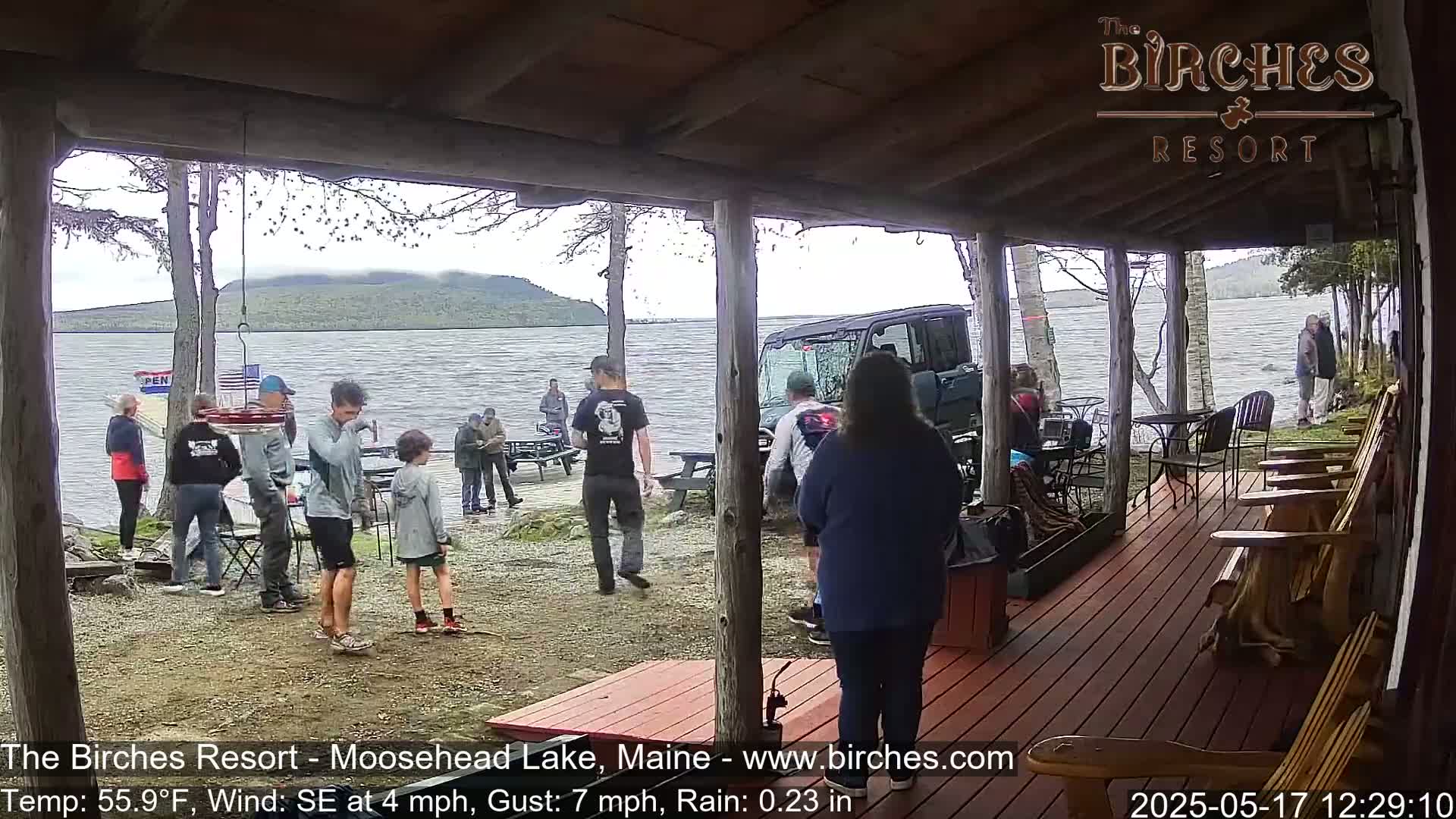 A group of people stand on a porch overlooking a lake on a rainy day, with a utility vehicle parked nearby.