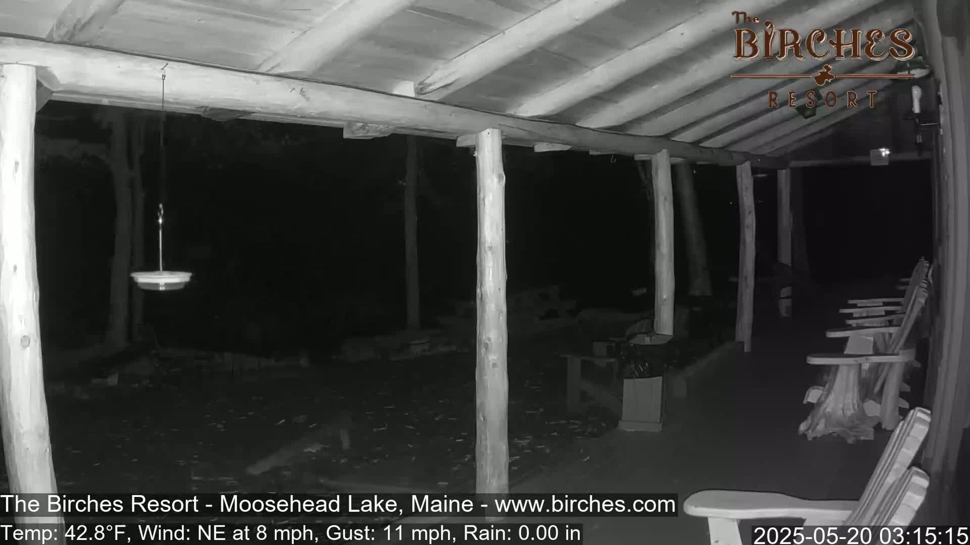 A nighttime, rainless scene shows a covered porch with wooden posts and chairs, and a bird feeder hanging from the ceiling; a northeast wind is blowing at eight miles per hour with gusts up to eleven.