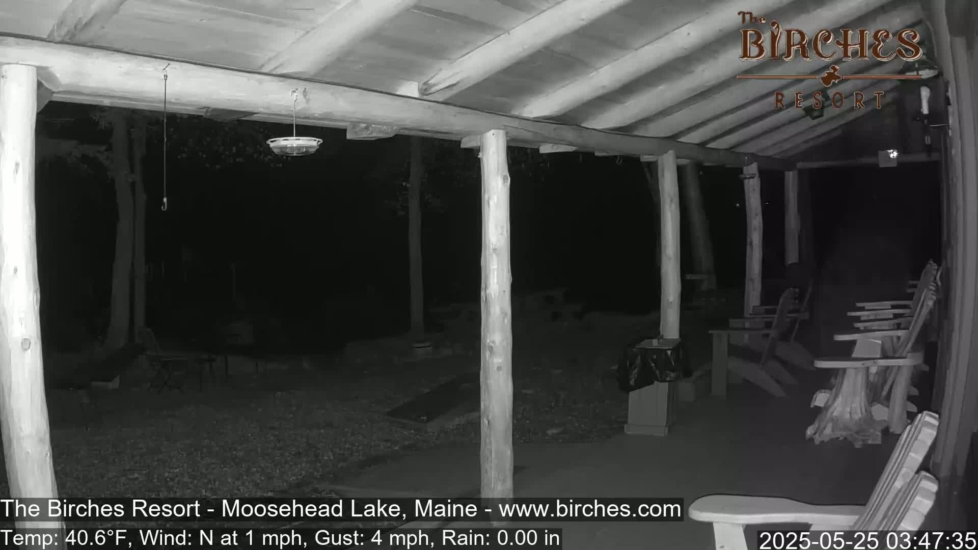 A nighttime, low-light image shows a covered porch with wooden posts and several Adirondack chairs, under a mostly clear sky with a light north wind.