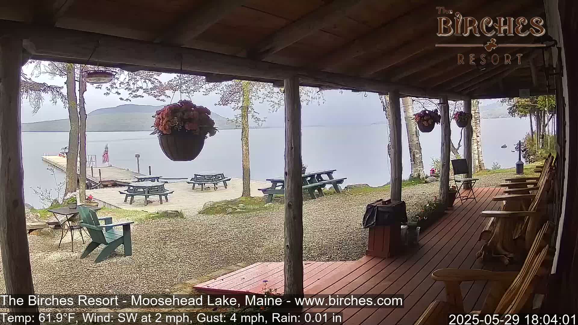 A porch overlooks a lake with picnic tables and a dock under lightly rainy conditions.