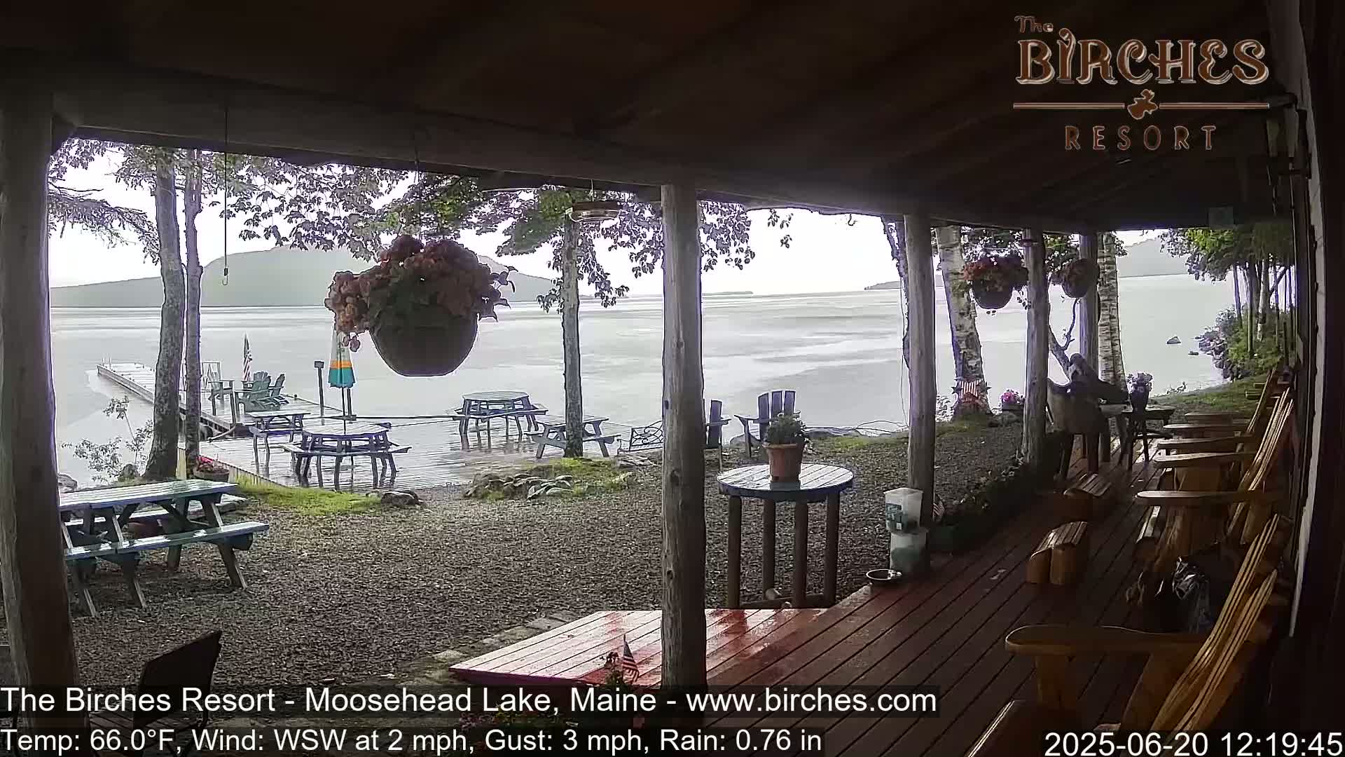 A covered porch overlooks a rainy lake with picnic tables and Adirondack chairs scattered on the patio and dock.