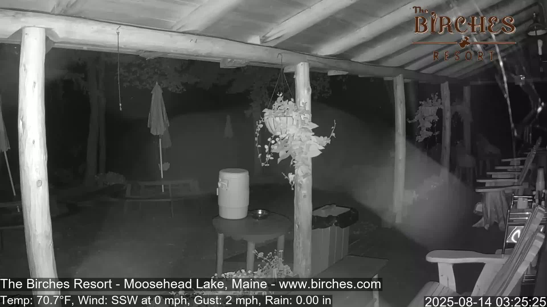 A nighttime view of a covered porch with outdoor furniture, potted plants, and a cooler, under calm, clear conditions.