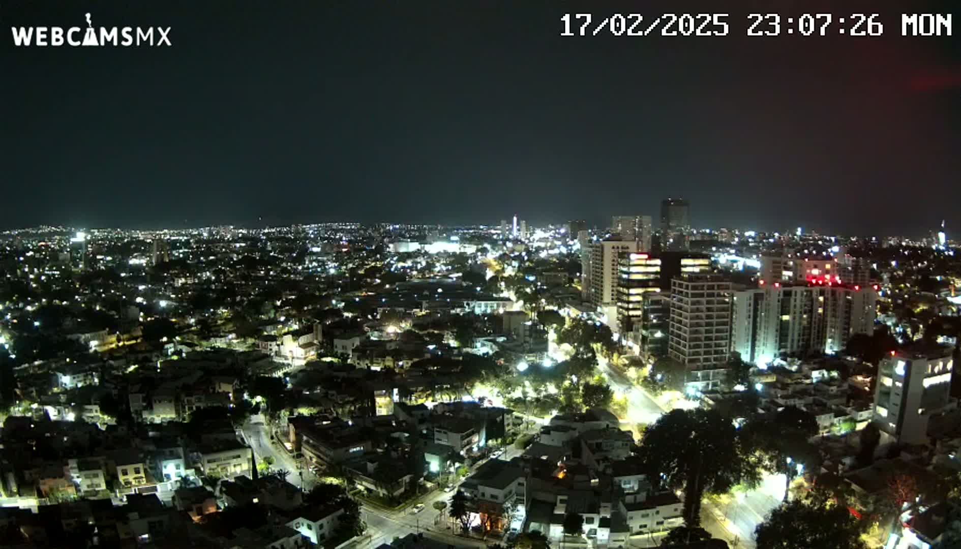 A nighttime aerial view of a city, with many buildings lit up under a clear, dark sky.