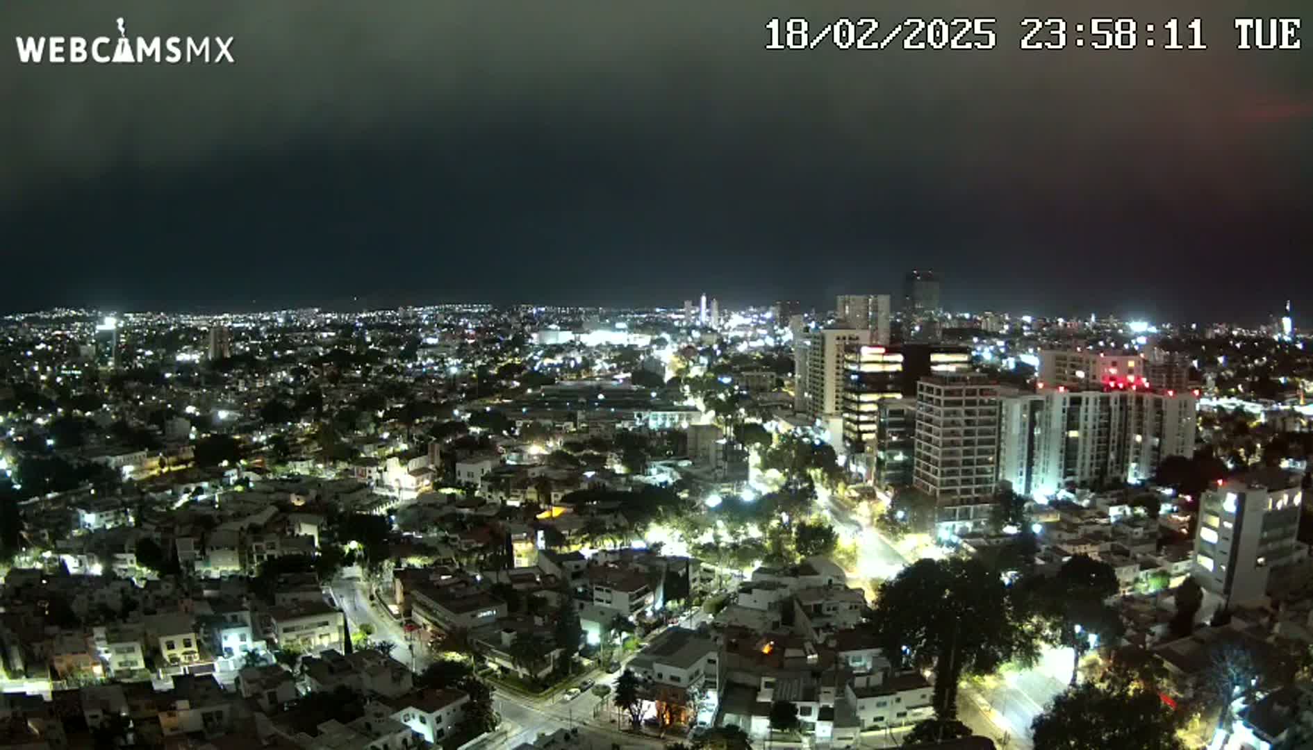 A nighttime, high-angle view of a sprawling city illuminated by streetlights and building lights under a dark, cloudy sky.