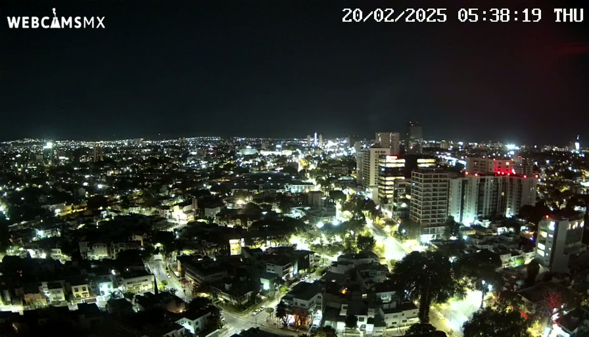 A nighttime aerial view of a sprawling city illuminated by streetlights and building lights under a clear sky.