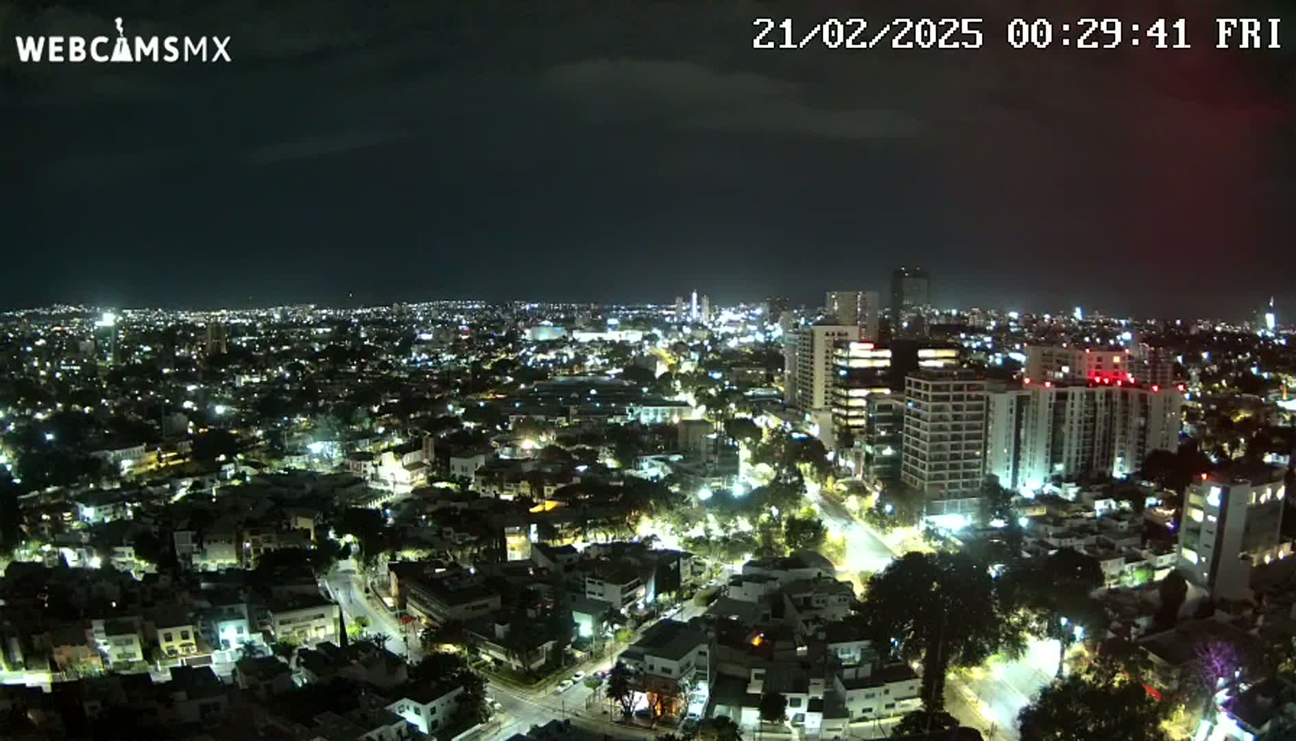 A nighttime, aerial view of a city with numerous buildings illuminated, under a mostly clear sky.